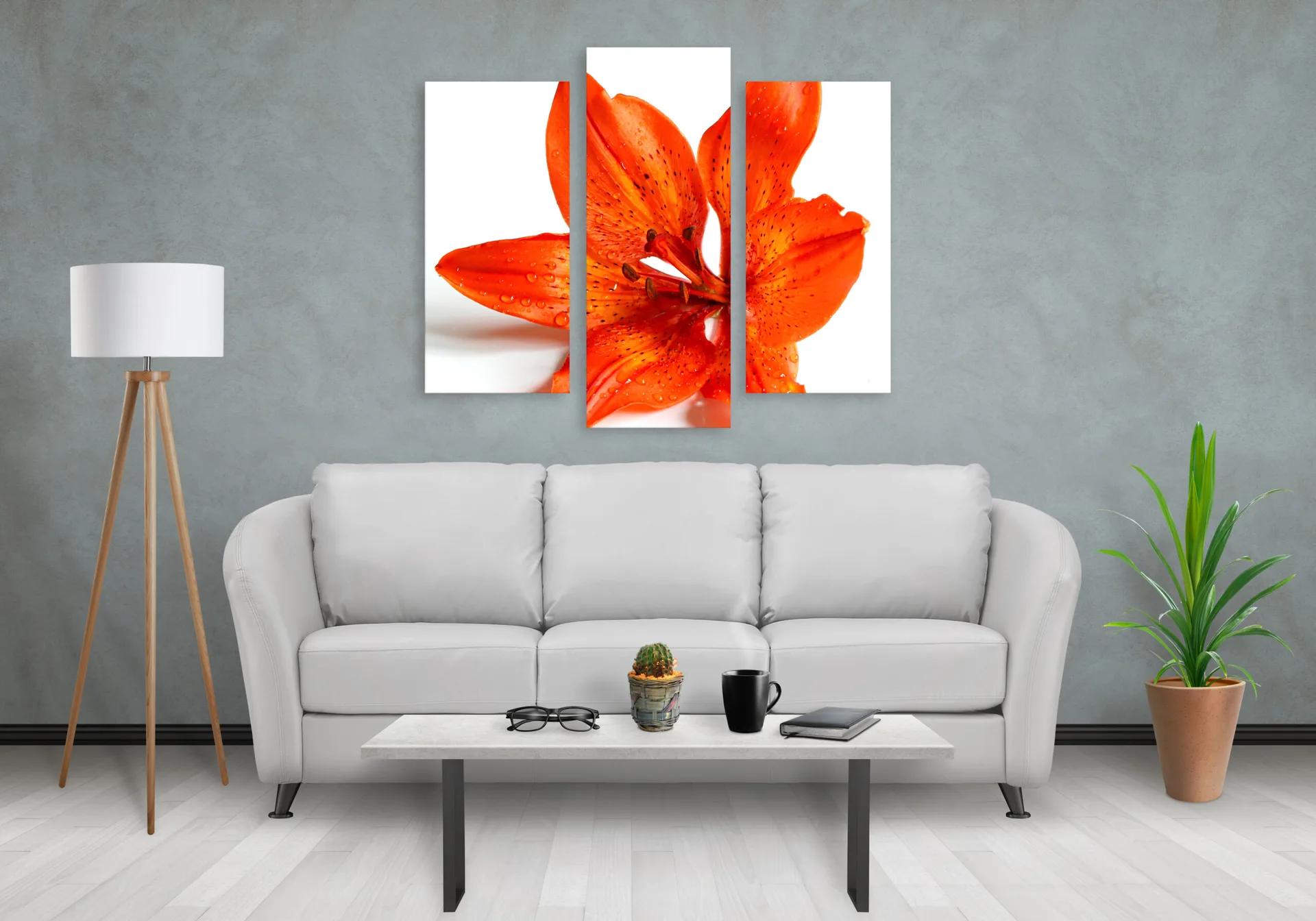 A gray-walled living room features a white sofa, a tripod floor lamp, a potted plant, and a large three-panel orange lily canvas print.