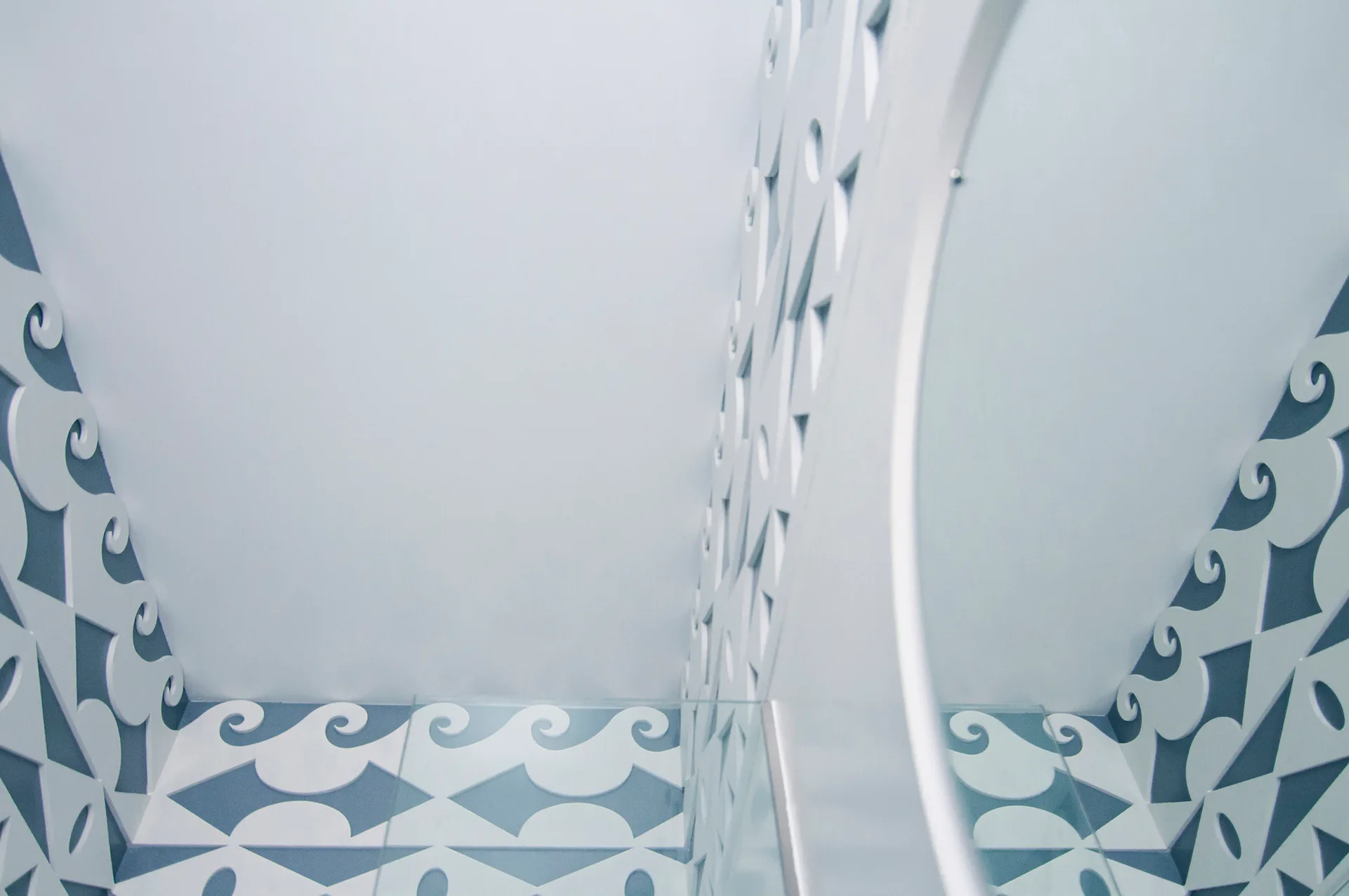 White decorative wall panels with a scrolled wave pattern overlay a blue background next to a round mirror reflecting the pattern.