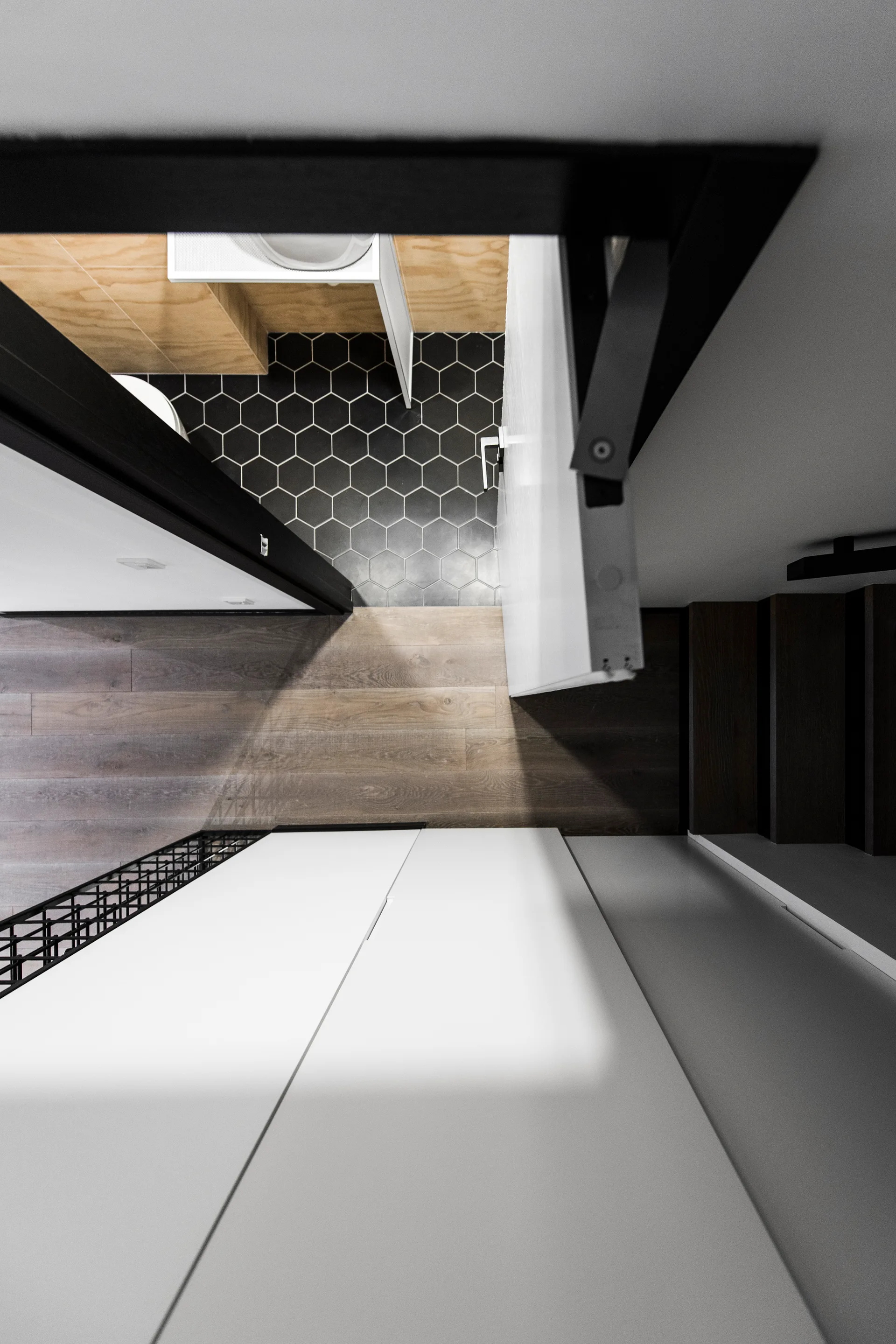 A top-down view shows an open white door leading into a bathroom with black hexagonal floor tiles and wood walls next to white hallway cabinets.