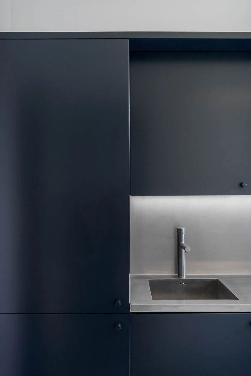 Matte charcoal kitchen cabinets surround an integrated stainless steel sink and matching backsplash illuminated by under-cabinet lighting.