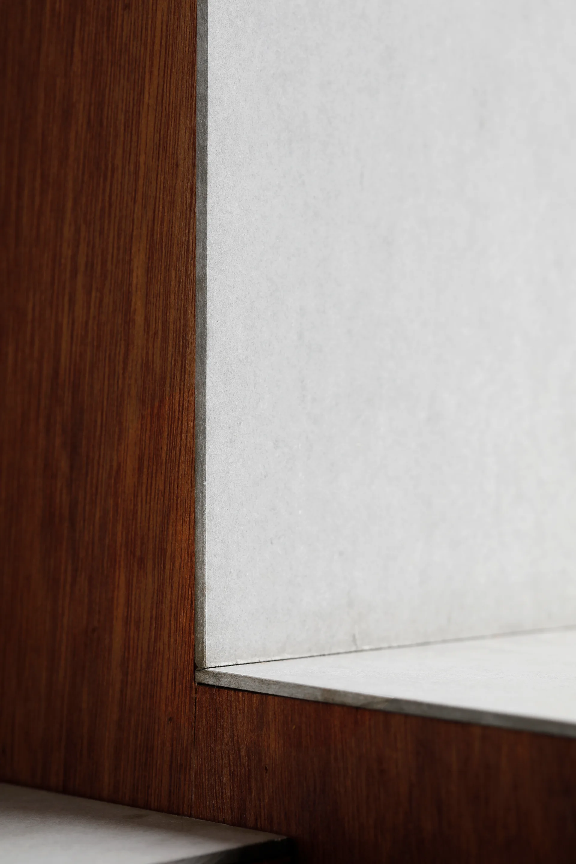 A close-up architectural detail showing the clean, flush junction where warm dark brown wood paneling meets a light grey matte stone surface.