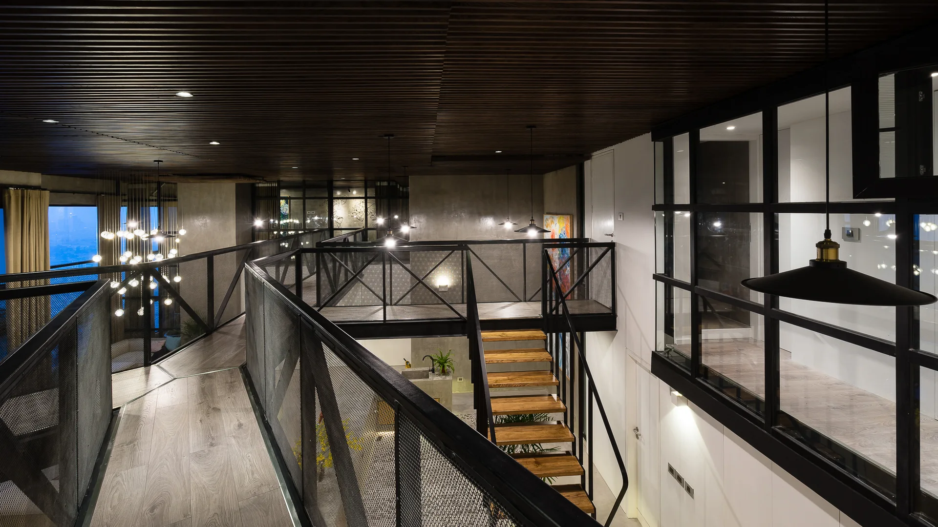 An industrial loft interior featuring a wood-plank mezzanine walkway, black metal mesh railings, an open-riser staircase, and a dark slatted wood ceiling.