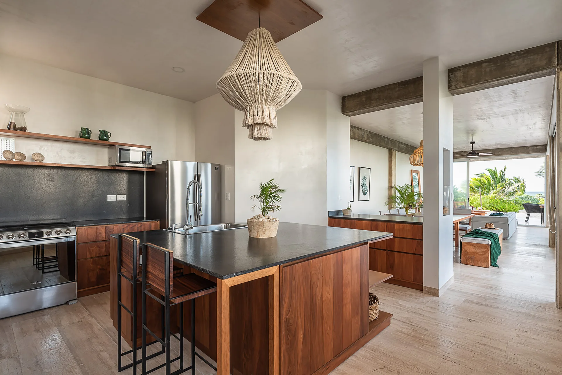 A modern kitchen featuring warm wood cabinetry, a dark countertop island, and a large woven pendant light hanging from a plaster ceiling.