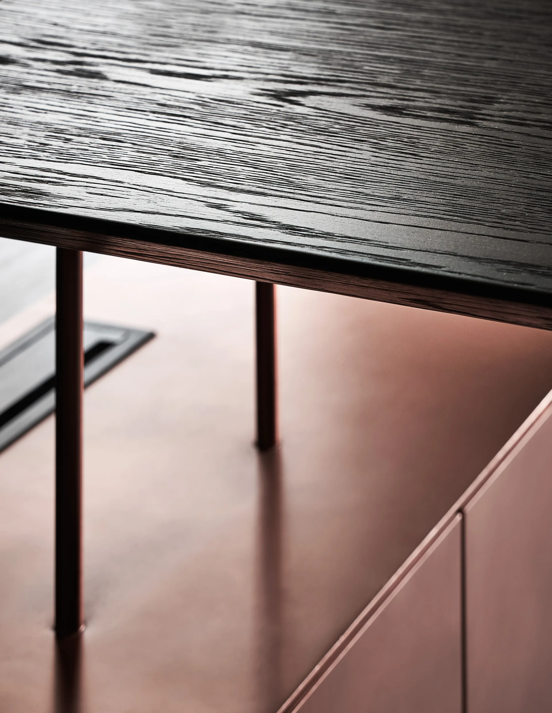 A close-up of a black textured wood table top resting above smooth rose-gold metallic cabinets.