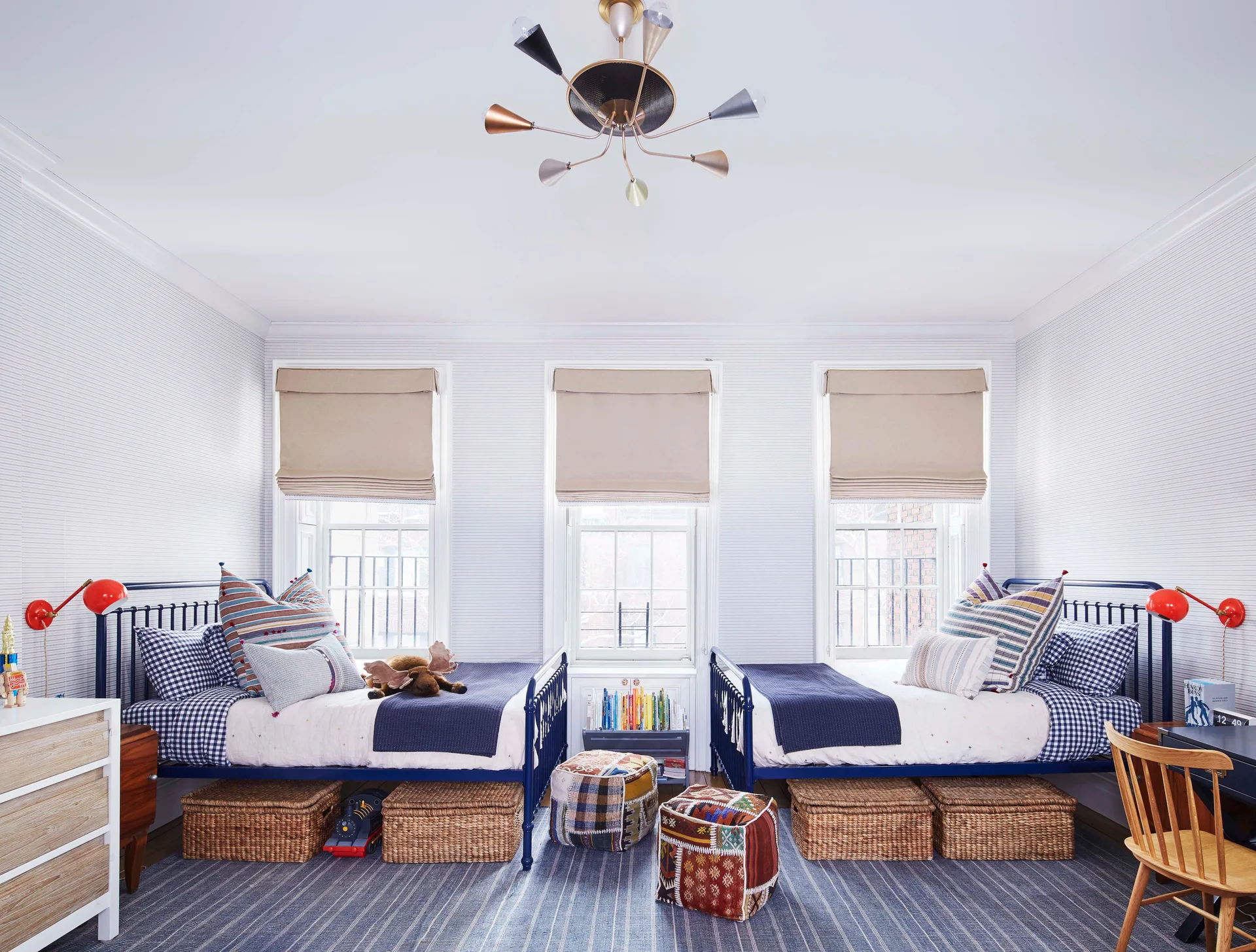A shared children's bedroom features two navy blue metal beds with woven storage baskets underneath, set against horizontal pinstriped wallpaper.