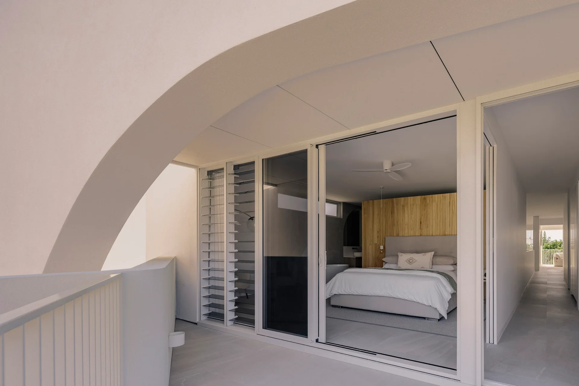 A view from a light gray patio through a sliding glass door into a bedroom featuring a vertical wood slat accent wall and a gray upholstered bed.