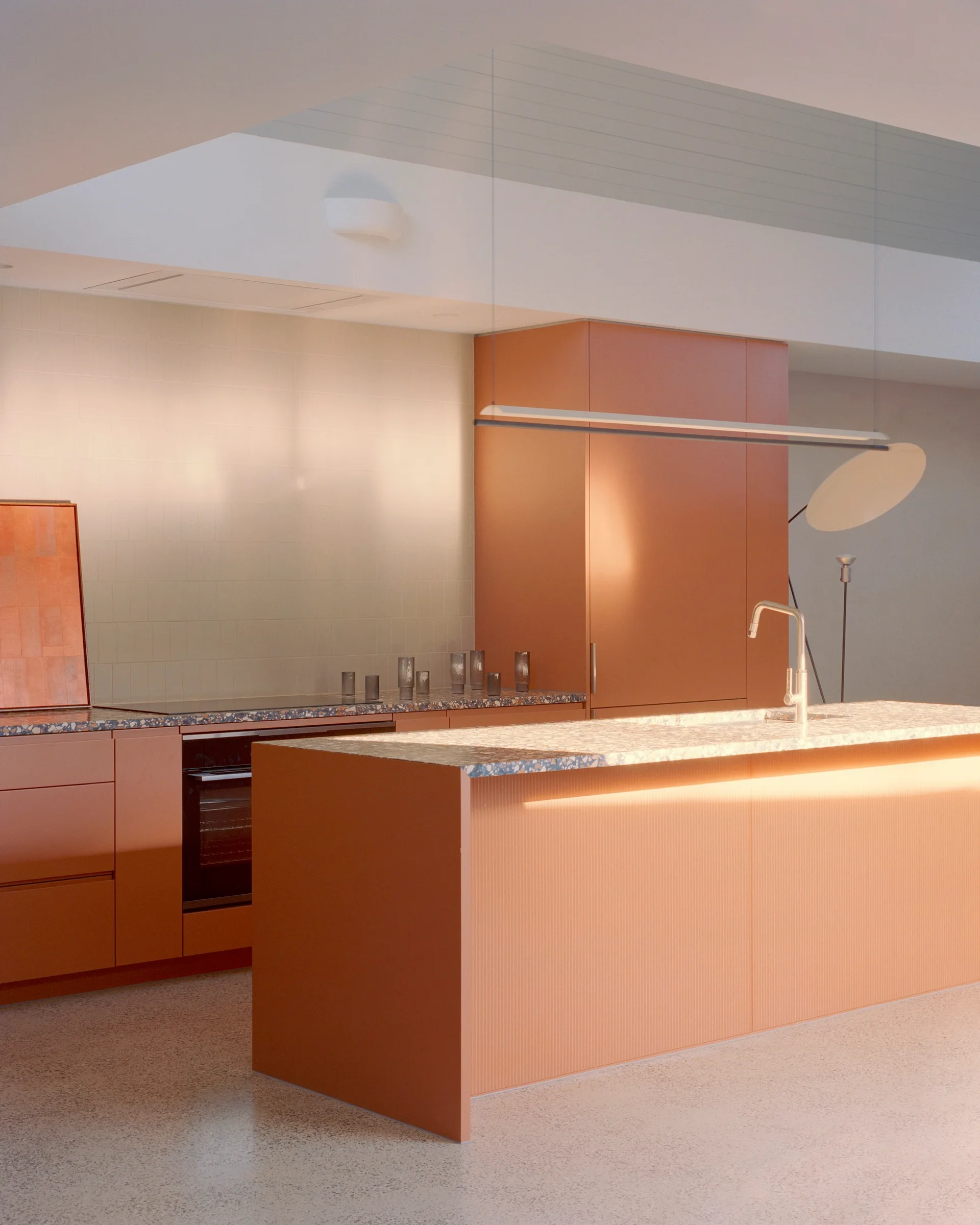 A modern kitchen featuring terracotta orange cabinetry, a ribbed kitchen island with a terrazzo countertop, an integrated oven, and a linear pendant light.