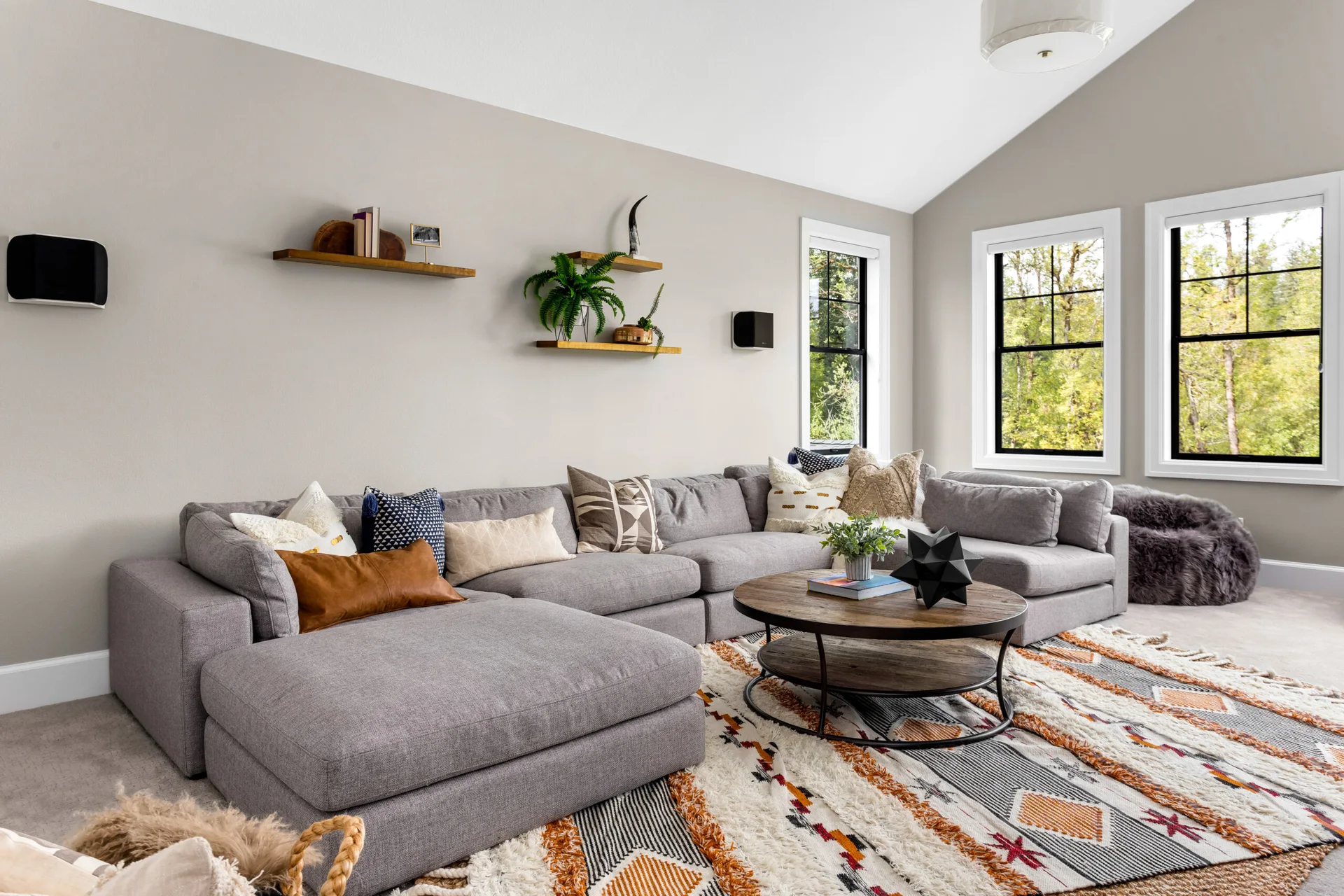 A cozy living room features a large grey sectional sofa, a round wooden coffee table, and a textured bohemian area rug.