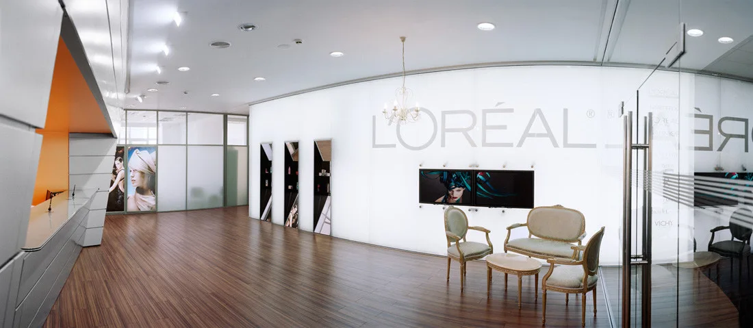 A corporate reception lobby features a sleek white desk, dark wood flooring, and classic seating set against a glowing backlit wall.