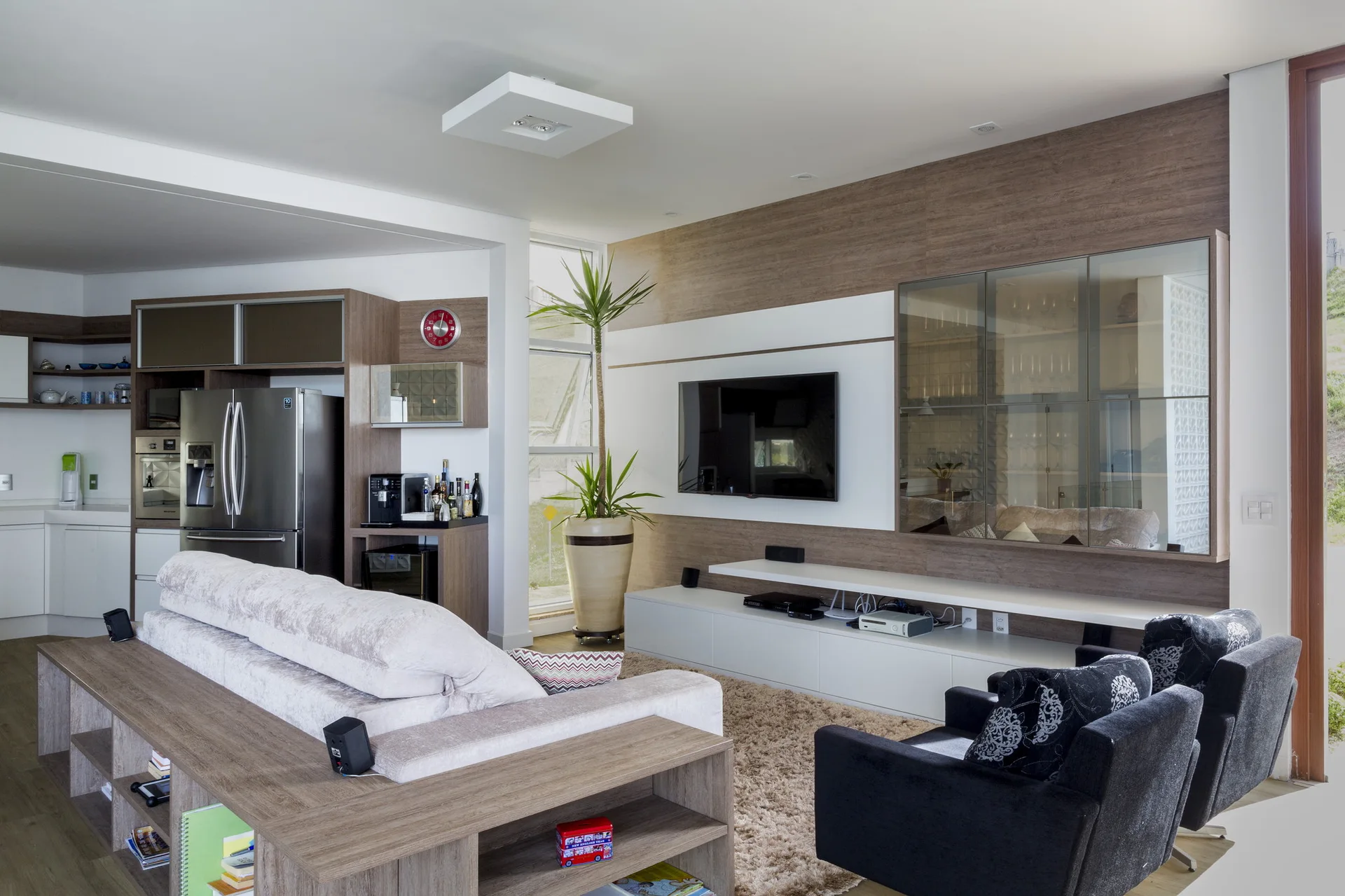 A contemporary open-plan living room features a wood-paneled wall unit with a TV, a low white media console, and a sofa with a console table behind it.