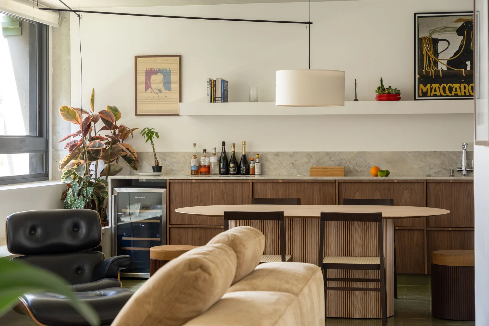 An open-concept dining space features an oval wood table with a slatted base, surrounded by dark wood chairs, under-counter cabinets, and a beige sofa.