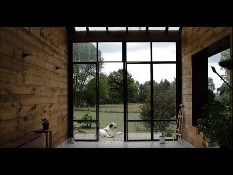 A sunroom features warm wood-planked walls, geometric patterned tile flooring, and large black metal-framed glass doors looking out to a green lawn.