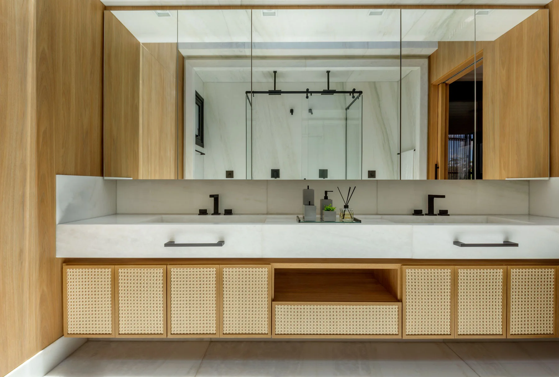A modern double bathroom vanity with wood cabinetry, woven cane door inserts, a white stone countertop, and two matte black faucets.