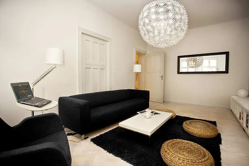 A modern black and white living room featuring a dark sofa, a shag rug, herringbone wood flooring, and a large white spherical pendant light.