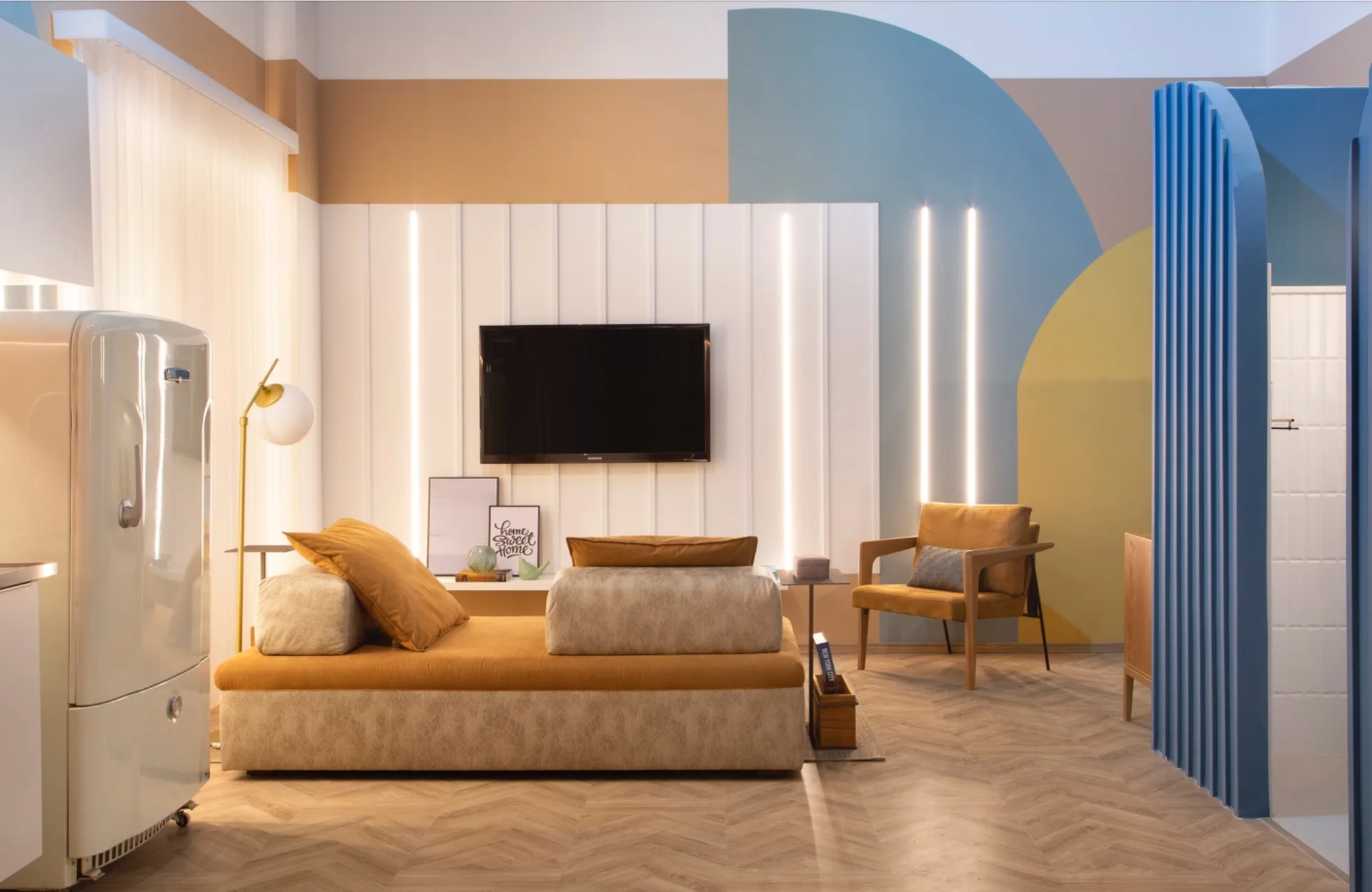 A living room featuring a mustard modular sofa, a wall-mounted TV on white paneling with vertical light strips, and a geometric-patterned wall.