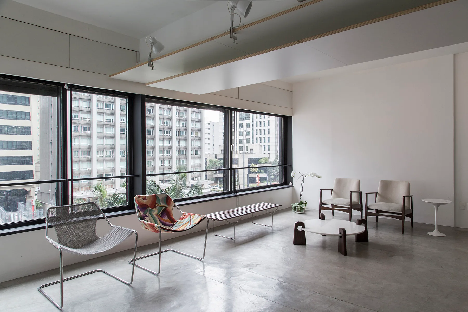 A minimalist living room features mixed modern armchairs, a low marble coffee table, polished concrete floors, and large windows with cityscape views.