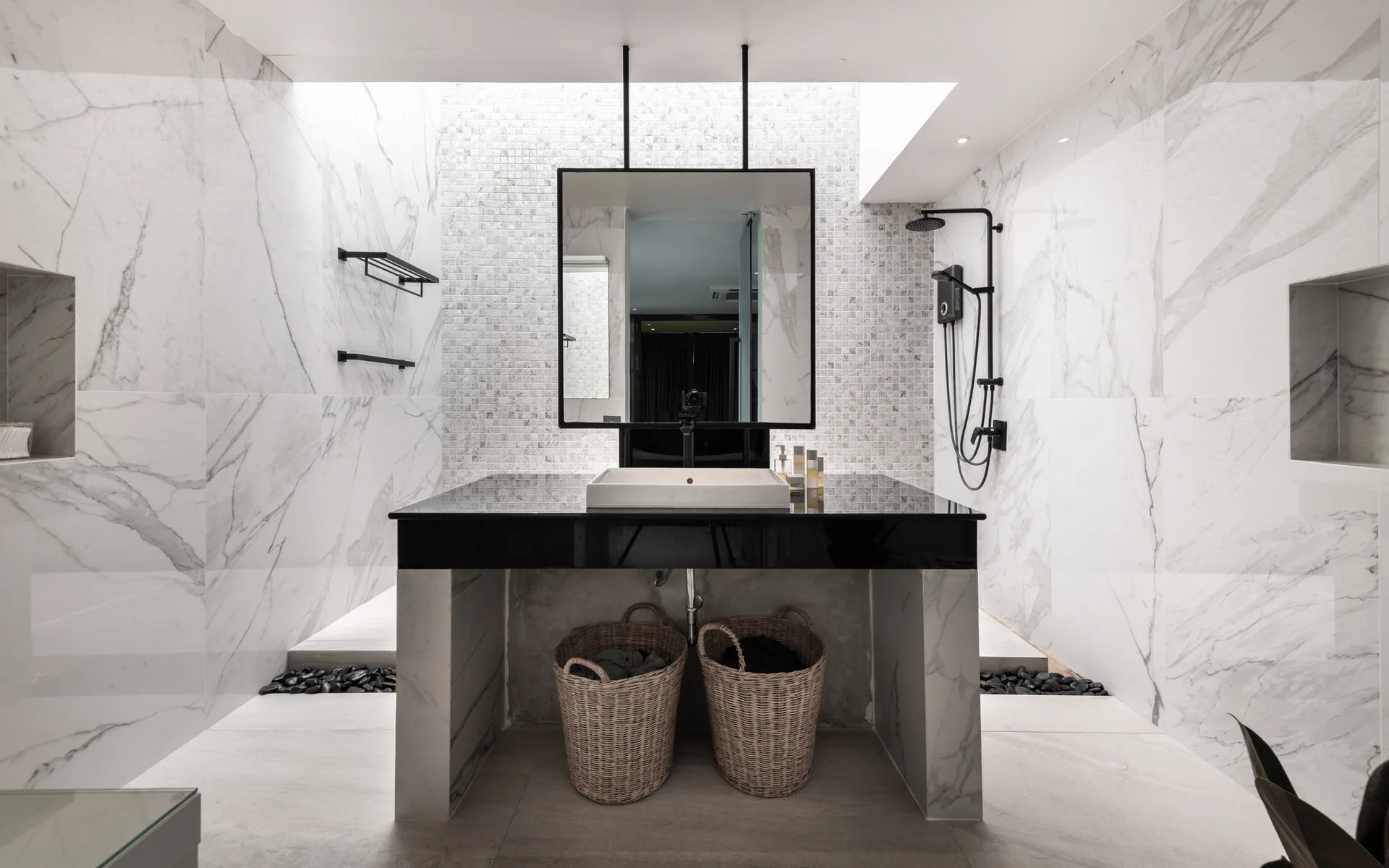 A modern bathroom features a central black vanity with a vessel sink, a black-framed mirror, and a mosaic tile accent wall flanked by marble slabs.