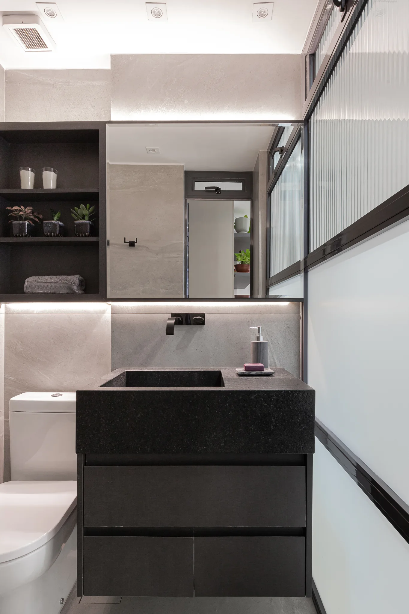 A modern bathroom features a dark black stone vanity with a wall-mounted faucet, a backlit mirror, and grey stone-patterned tiled walls.