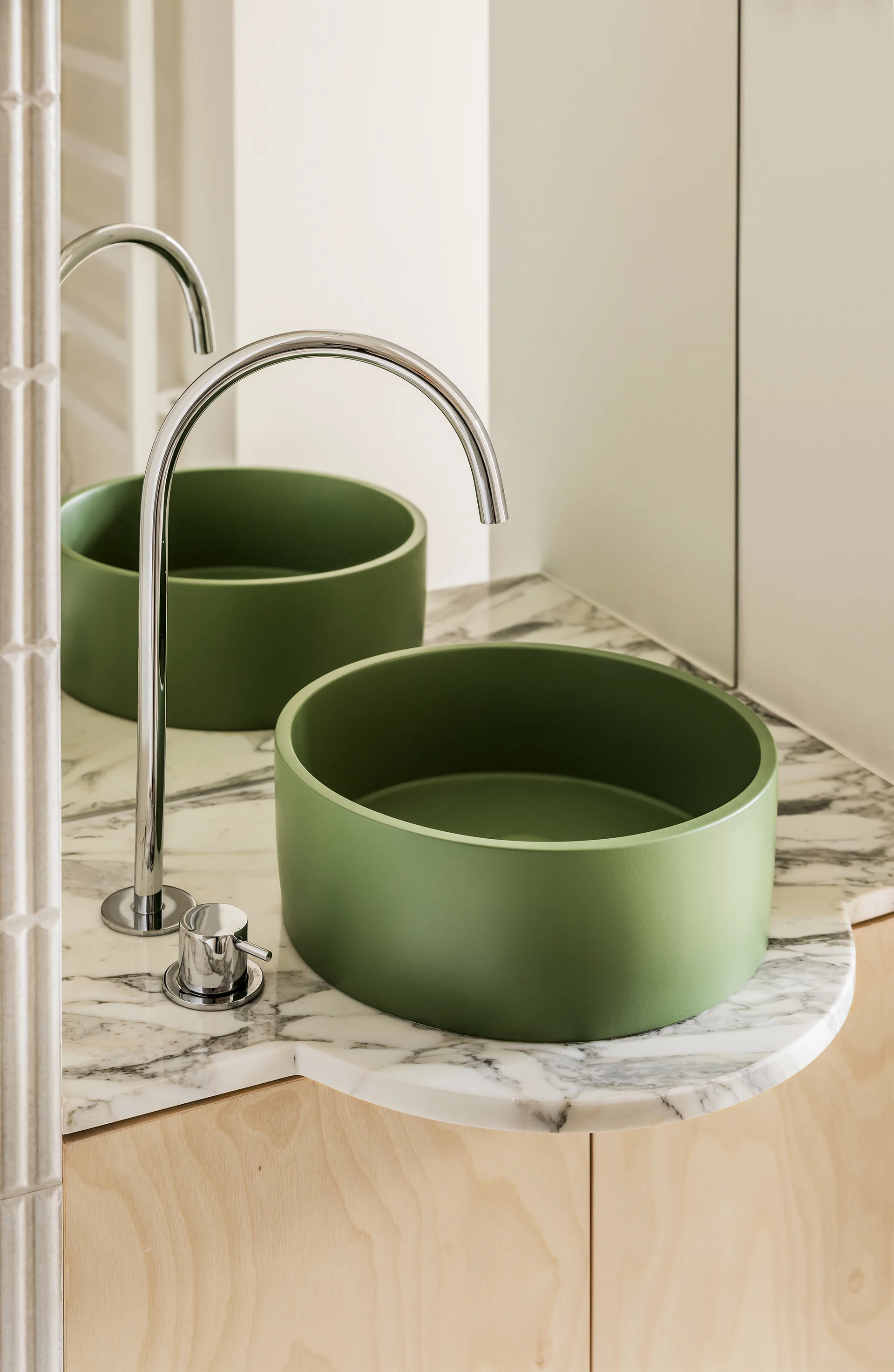 A circular matte green vessel sink sits on a curved white marble vanity top with a polished chrome faucet.
