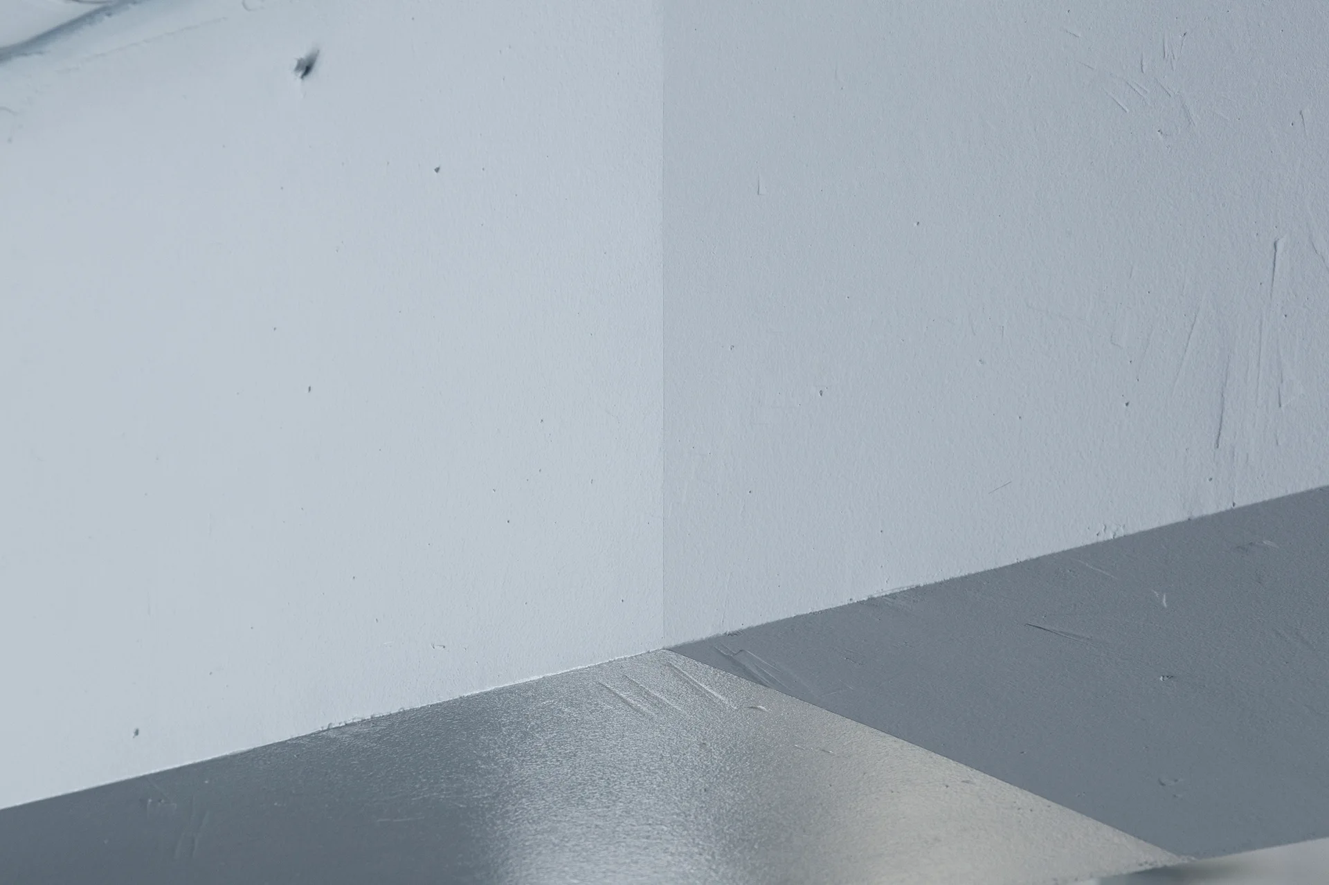 A close-up of a minimalist room corner featuring light grey painted walls and a medium grey floor.