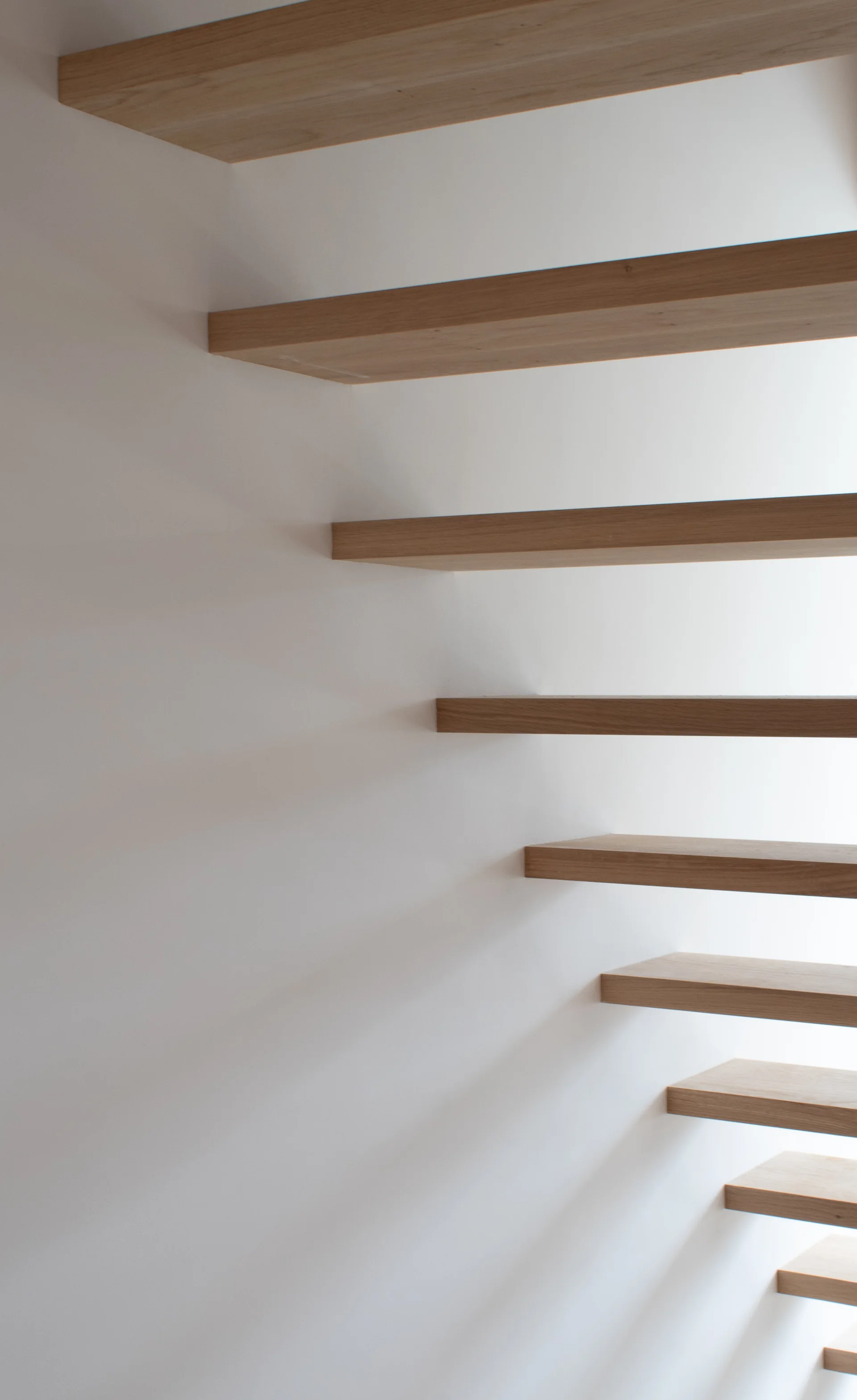 Floating light wood stair treads extend from a smooth white wall in a minimalist interior design.