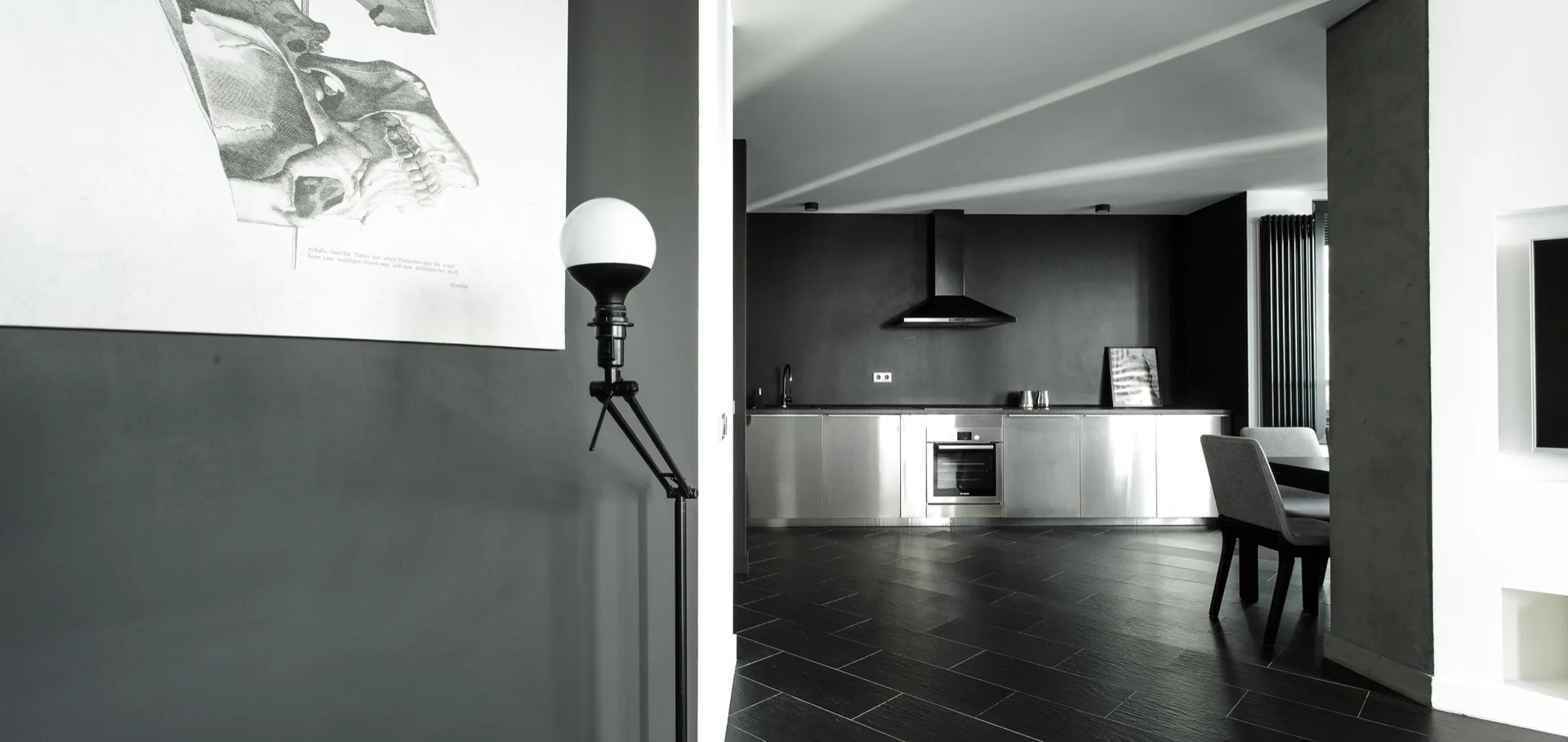A modern kitchen with stainless steel lower cabinets, a black range hood, matte dark grey walls, and black herringbone tile flooring.