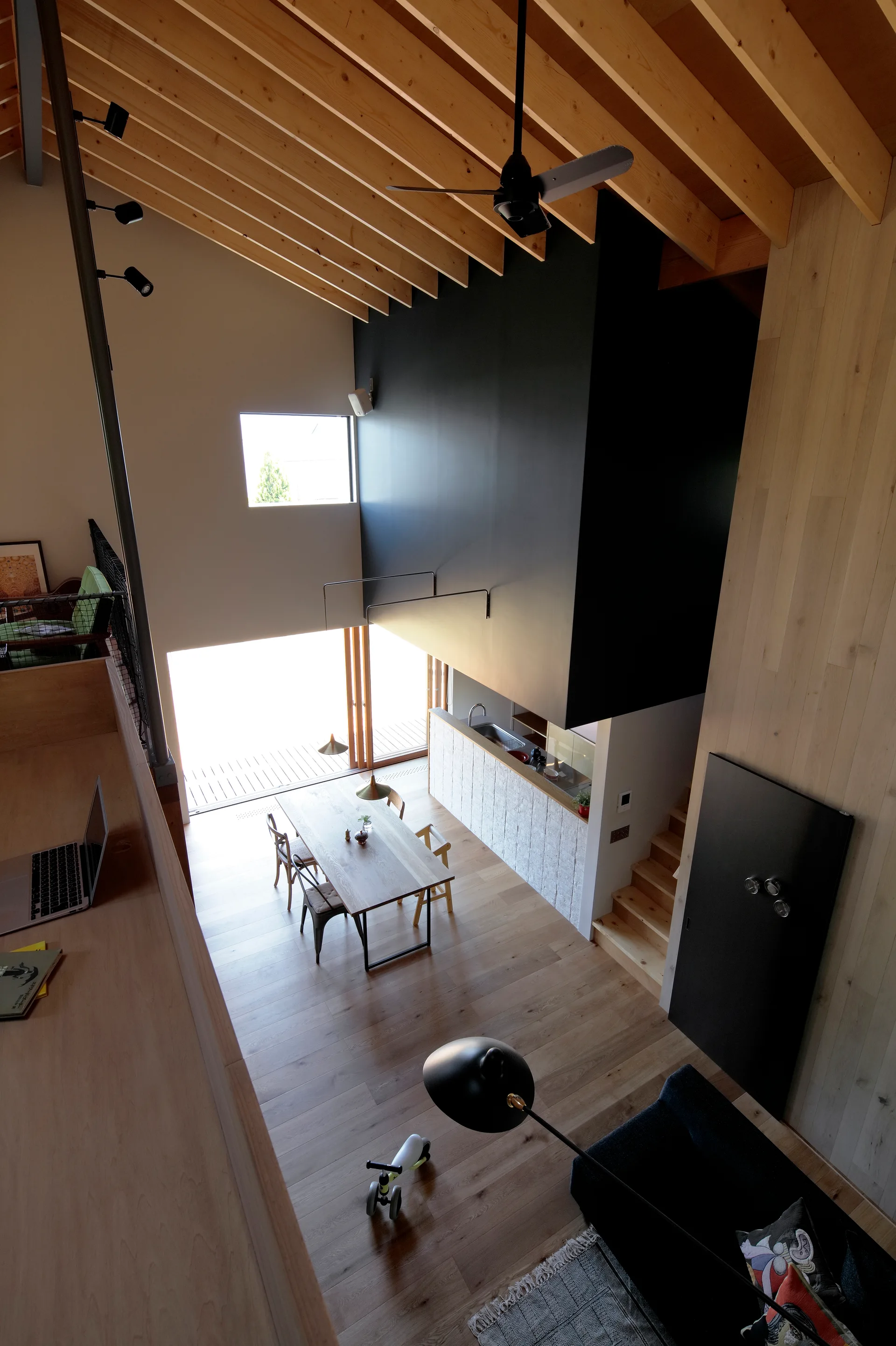 High-angle view of a modern wooden dining table below a vaulted ceiling with exposed wooden rafters and a large matte black architectural structure.