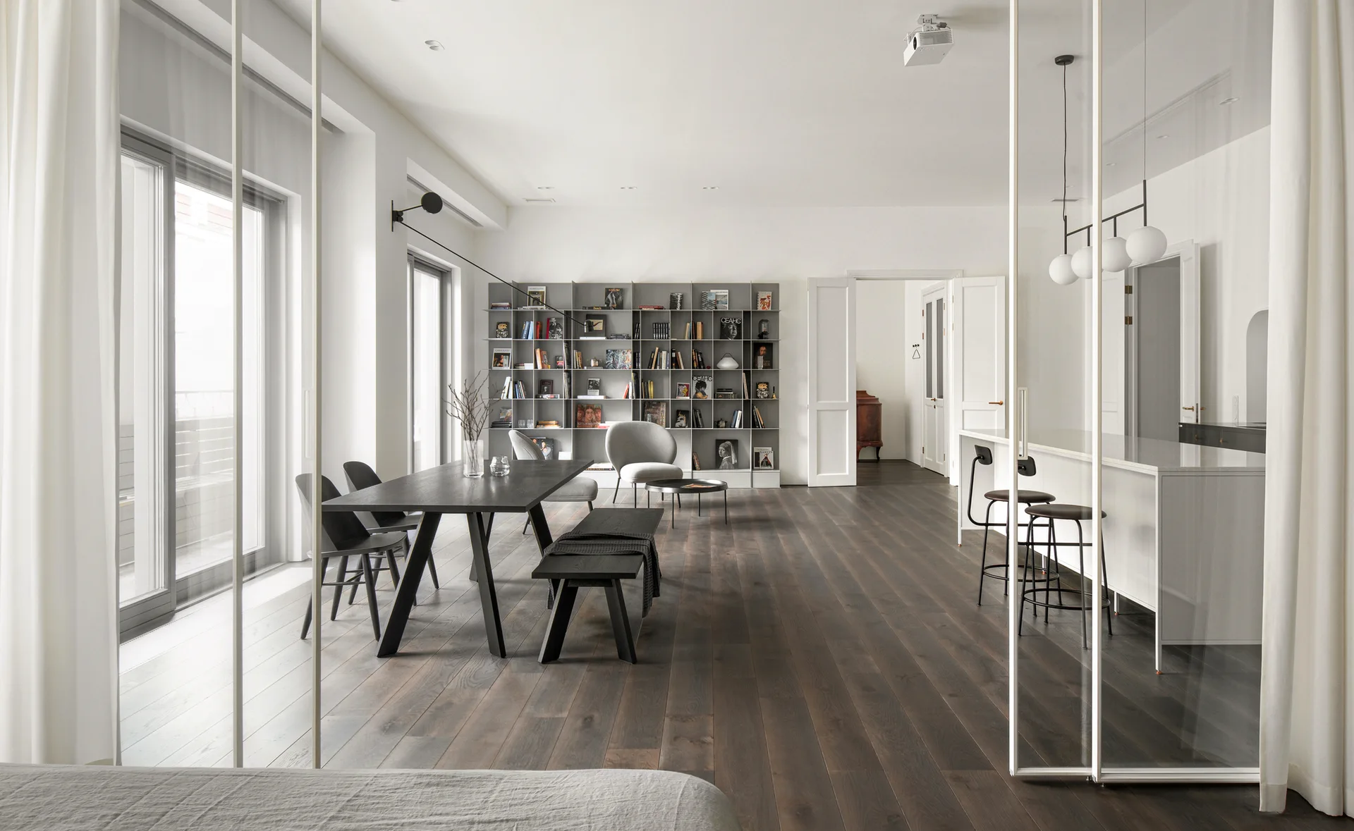 A minimalist open dining room featuring a black table, dark wood floors, a gray metal bookshelf, and sliding glass partition doors.