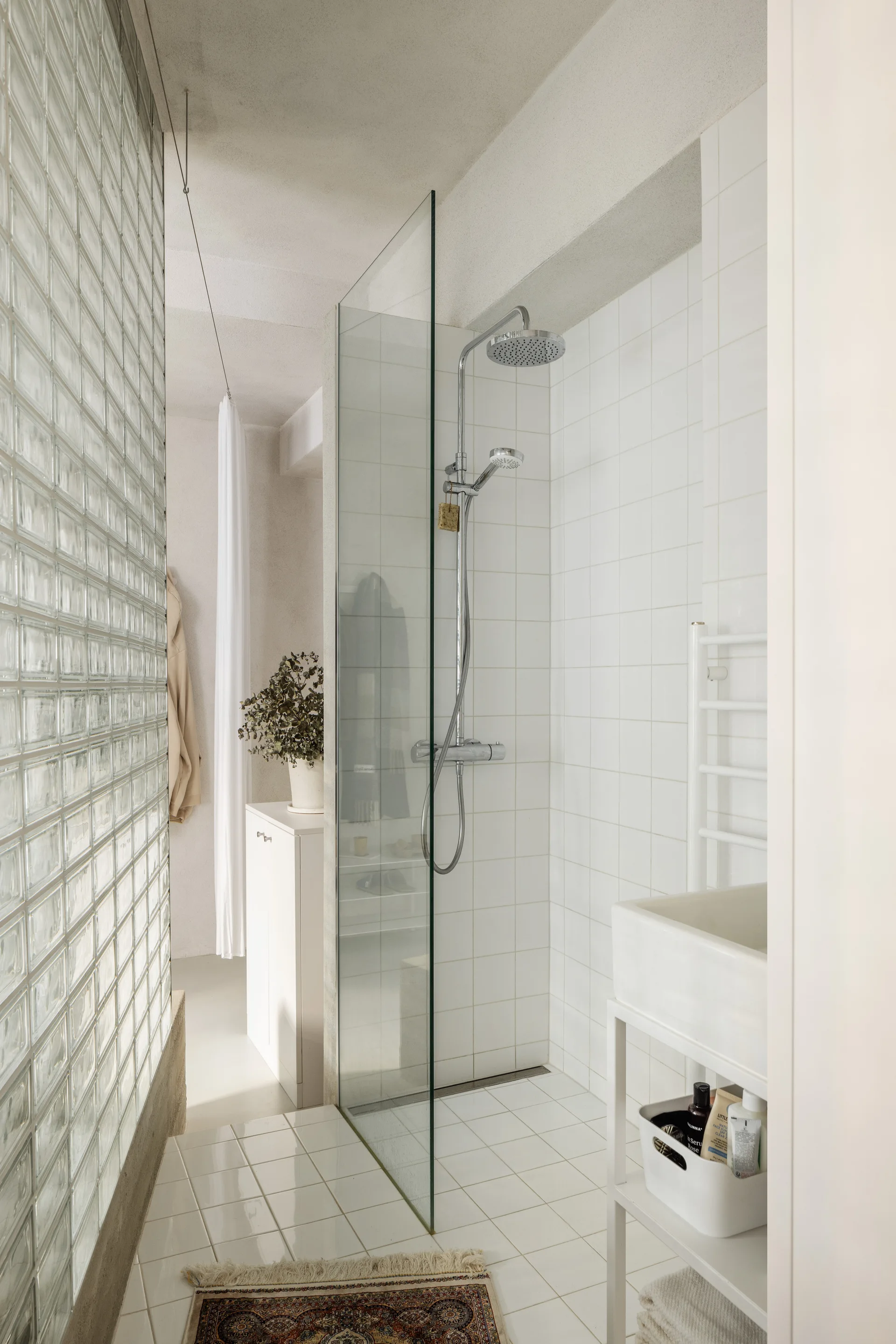 A minimalist white bathroom features a glass block partition wall next to a tiled shower with a glass panel and chrome fixtures.