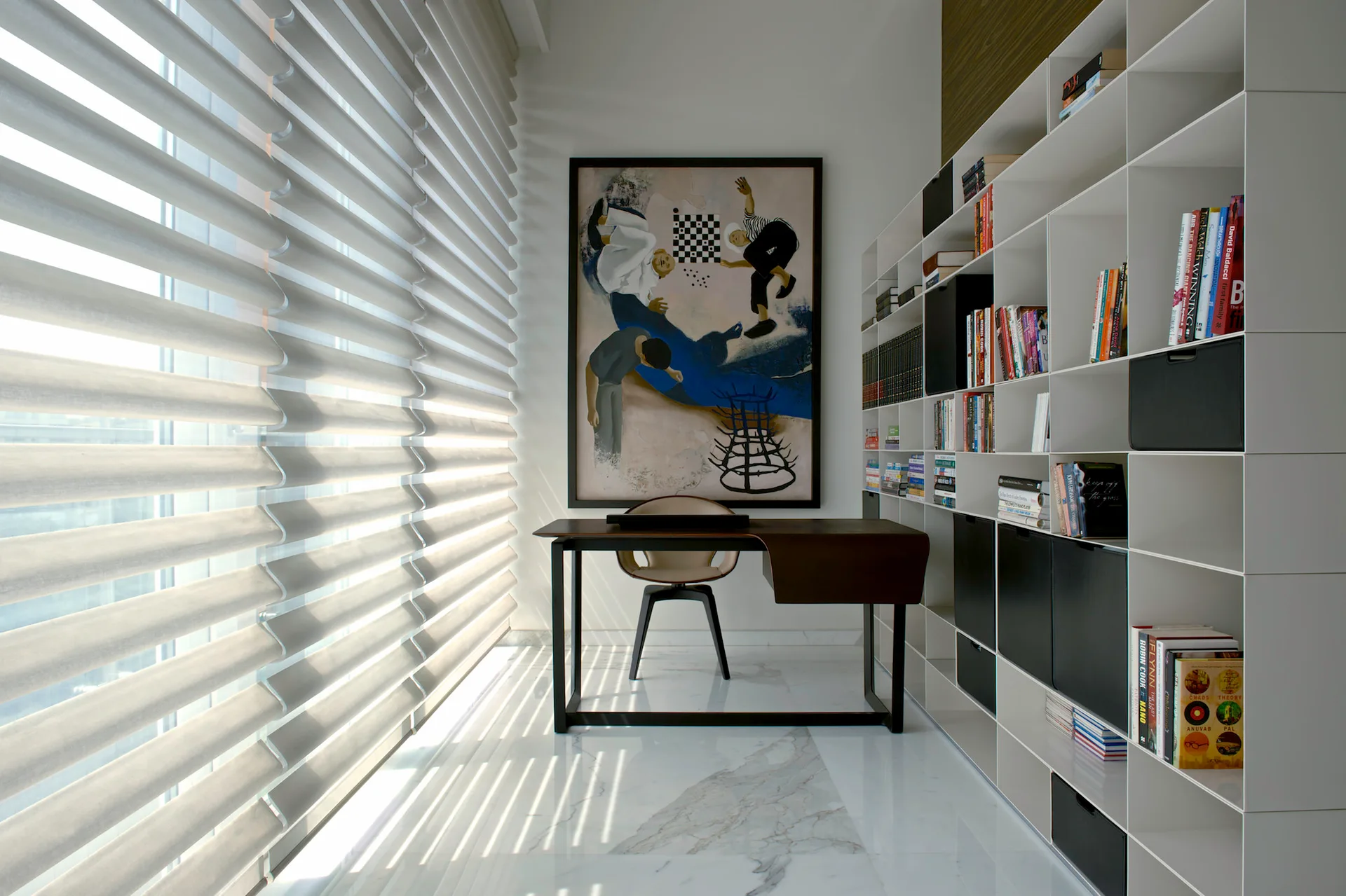 A modern home office featuring a dark wood desk, white modular shelving filled with books, a large abstract painting, and marble flooring.