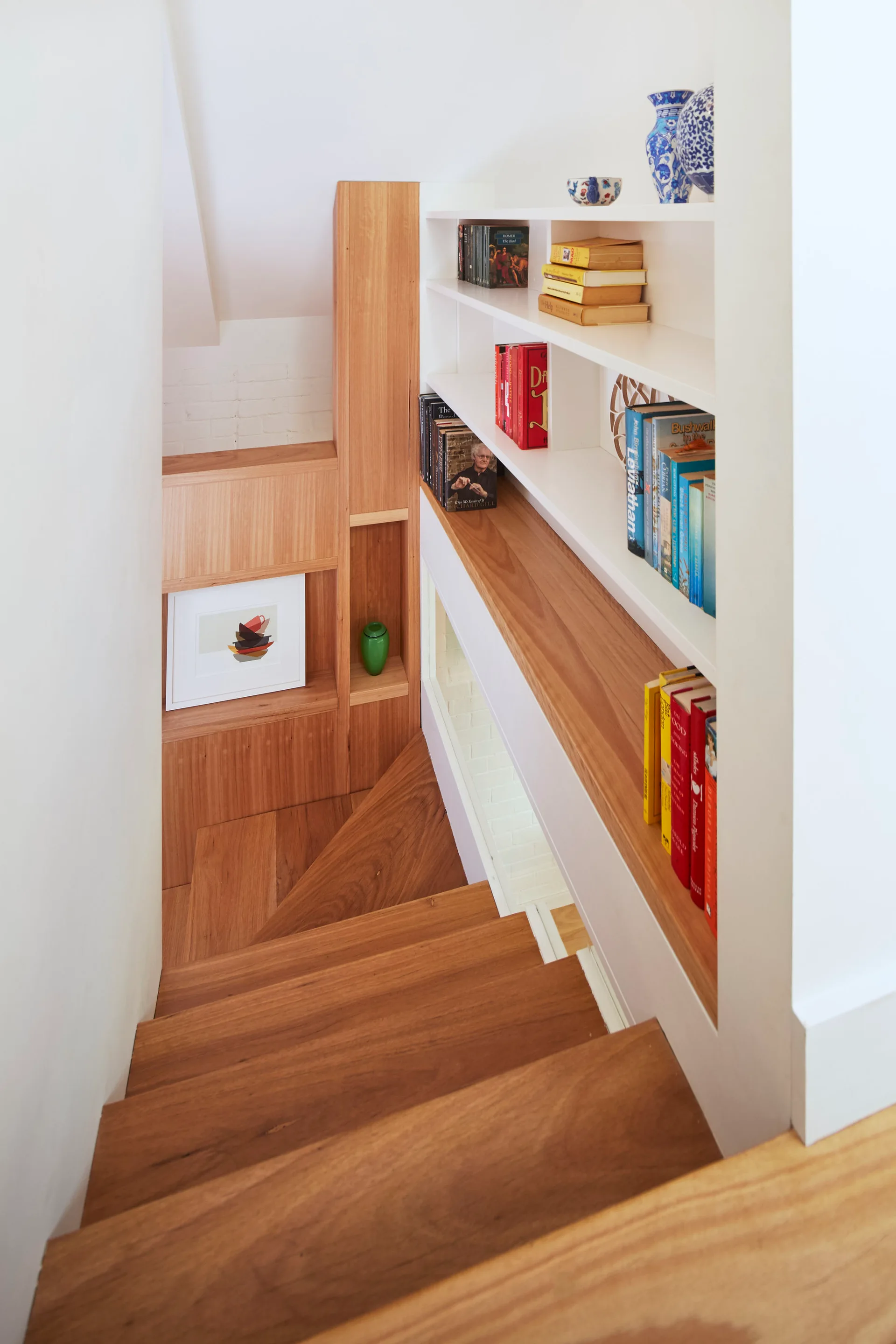 Looking down a wooden staircase next to a white recessed bookshelf filled with books and decorative vases.