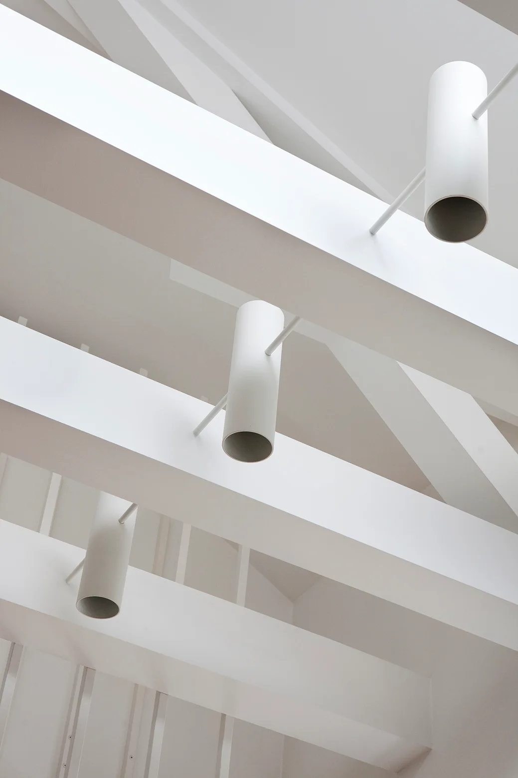Low-angle view of white painted ceiling beams interspersed with minimalist white cylindrical pendant lights.