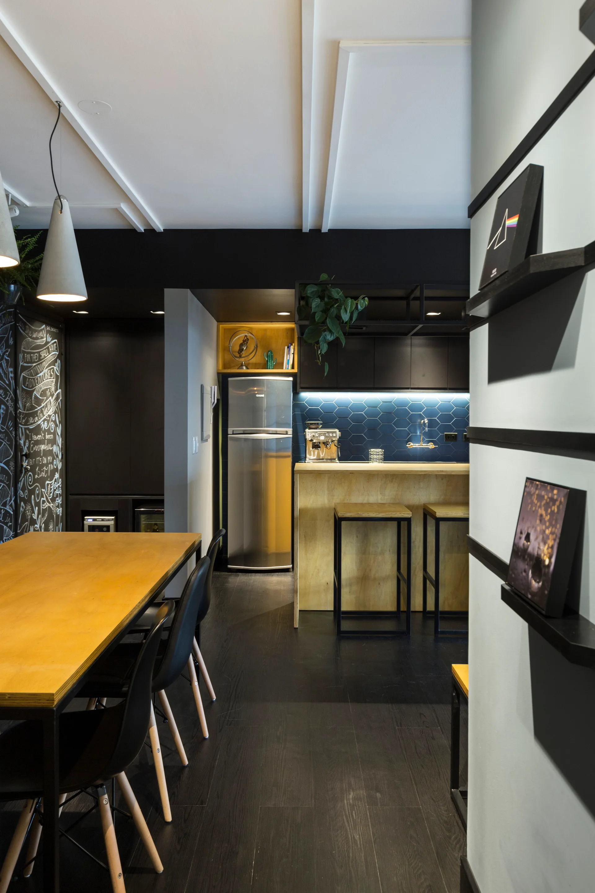Modern kitchen and dining area featuring a blue hexagonal tile backsplash, light wood bar counter, and matte black cabinetry with a dining table.