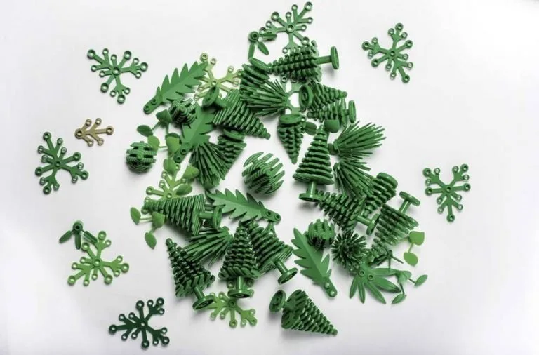 A flat lay collection of miniature green plastic toy trees and leaf-shaped botanical pieces scattered on a plain white background.