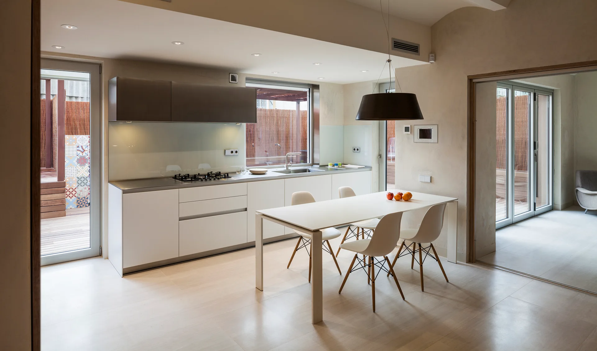 A modern kitchen featuring white flat-panel cabinetry, a stainless steel countertop, and a white dining table with molded chairs.