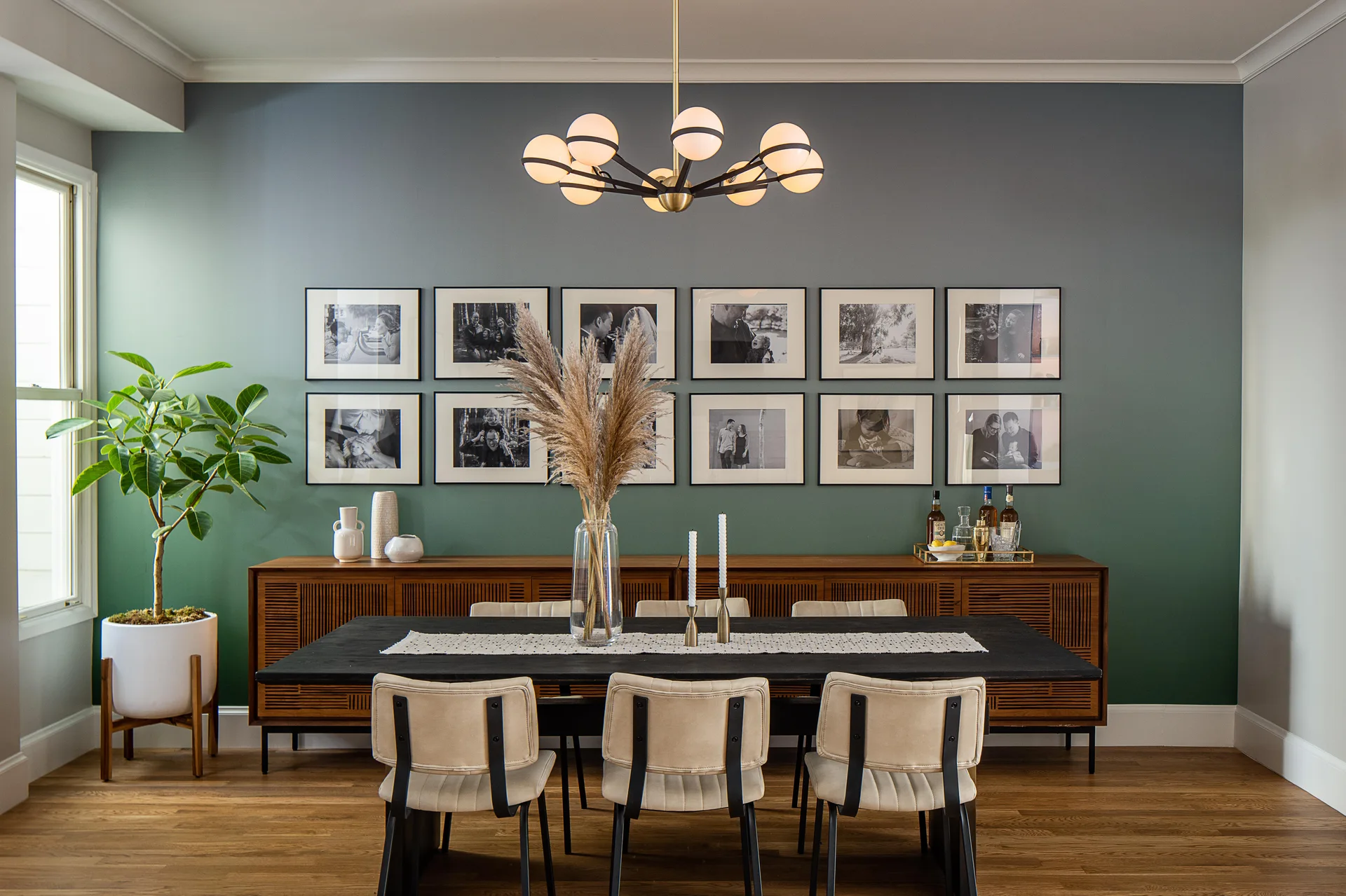 A contemporary dining room showing a black table, beige chairs, and a wood sideboard against a green-to-grey gradient wall with framed photos.