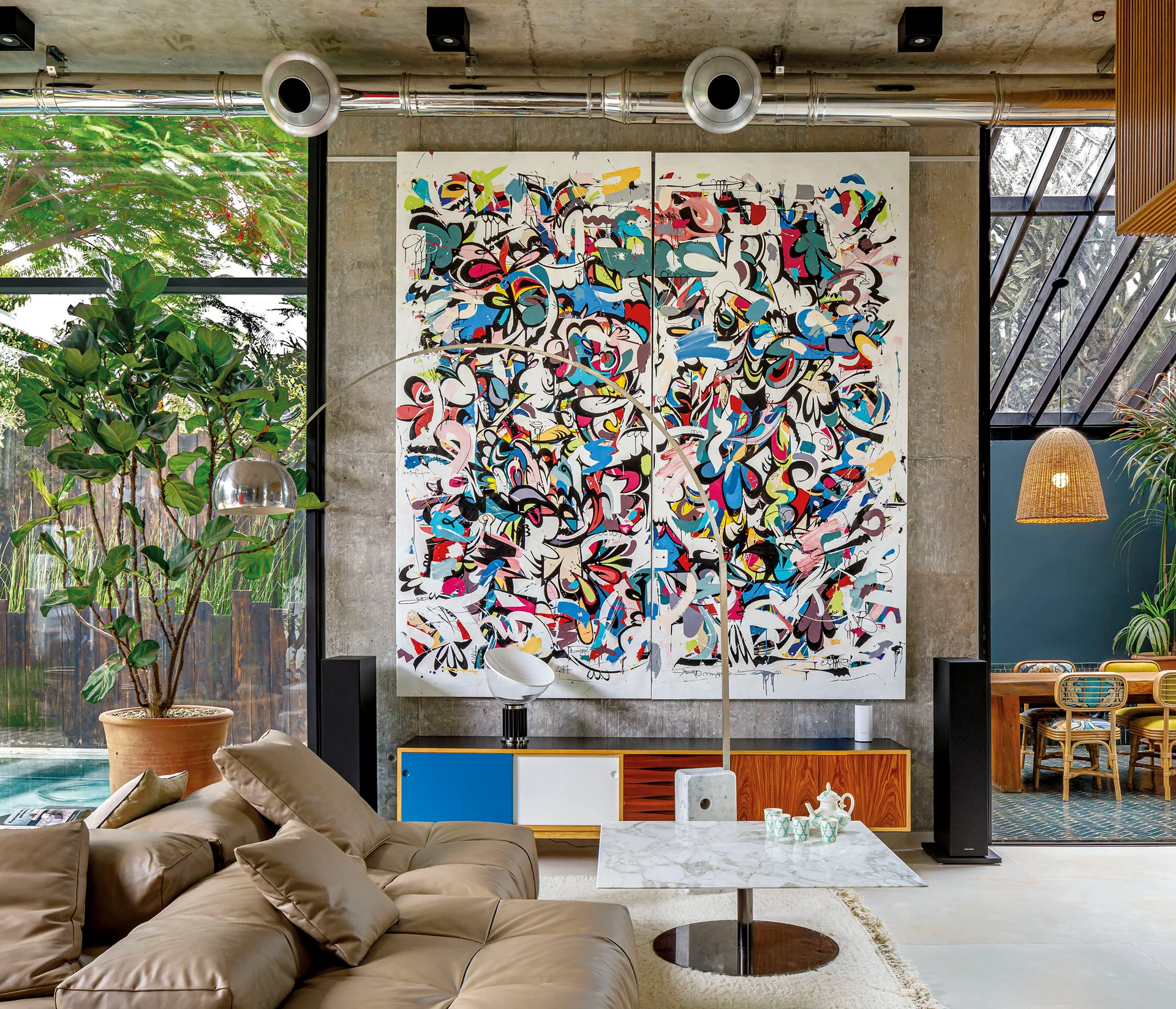 A contemporary living room features a tan leather sectional sofa, a marble coffee table, and a large abstract painting on an exposed concrete wall.