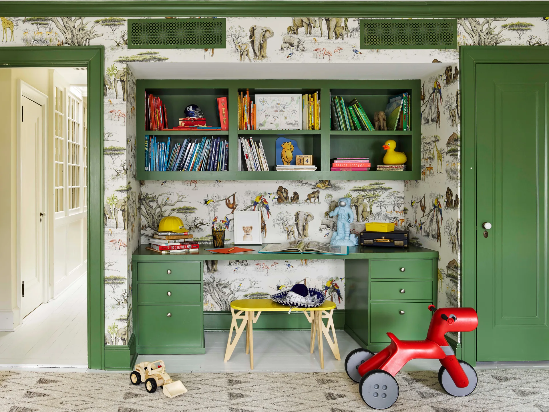 A forest green built-in desk and bookshelf unit is integrated into a wall niche with safari-themed wallpaper in a children's room.