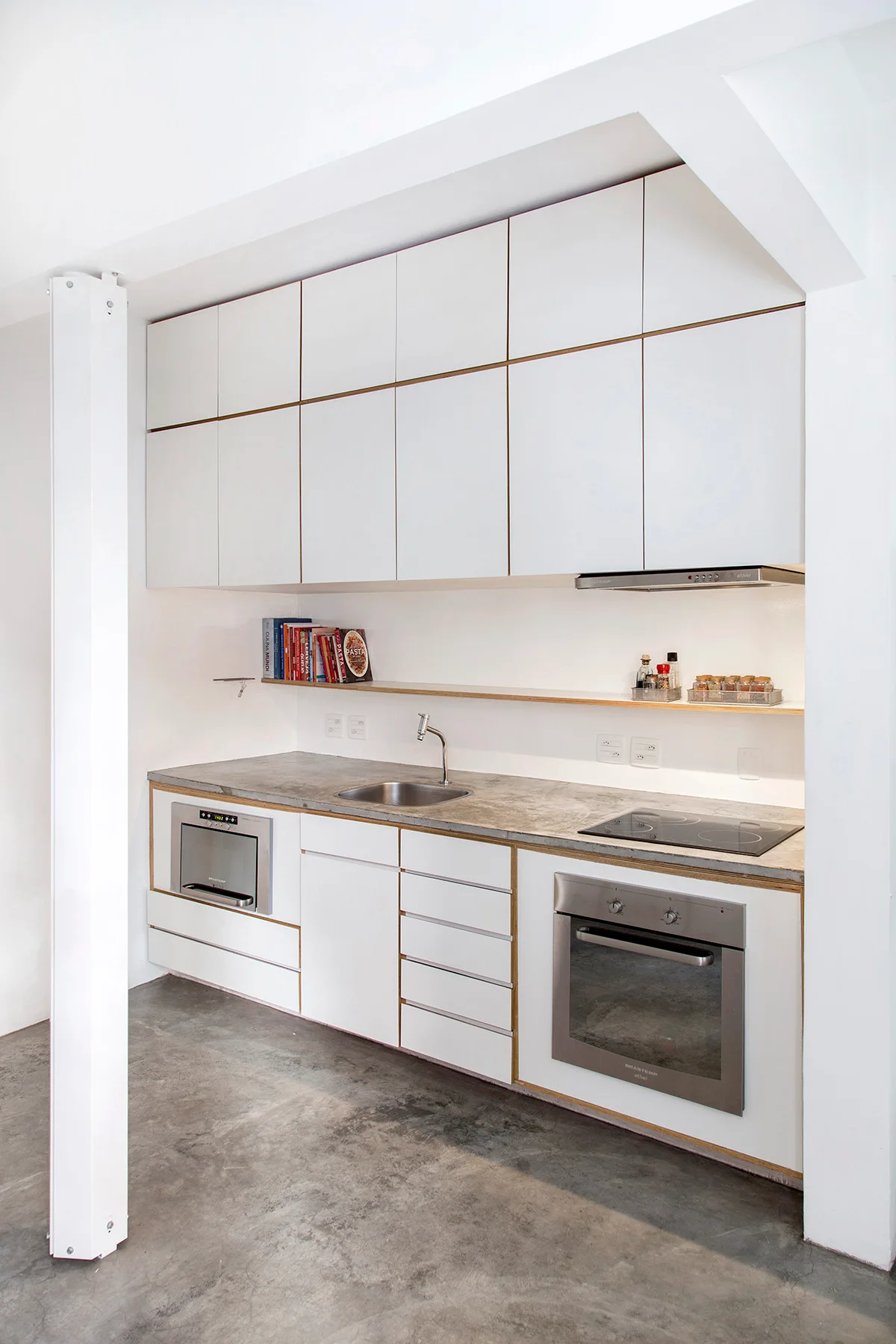 Minimalist kitchen featuring white cabinets with exposed plywood edges, a grey concrete countertop, and integrated stainless steel appliances.