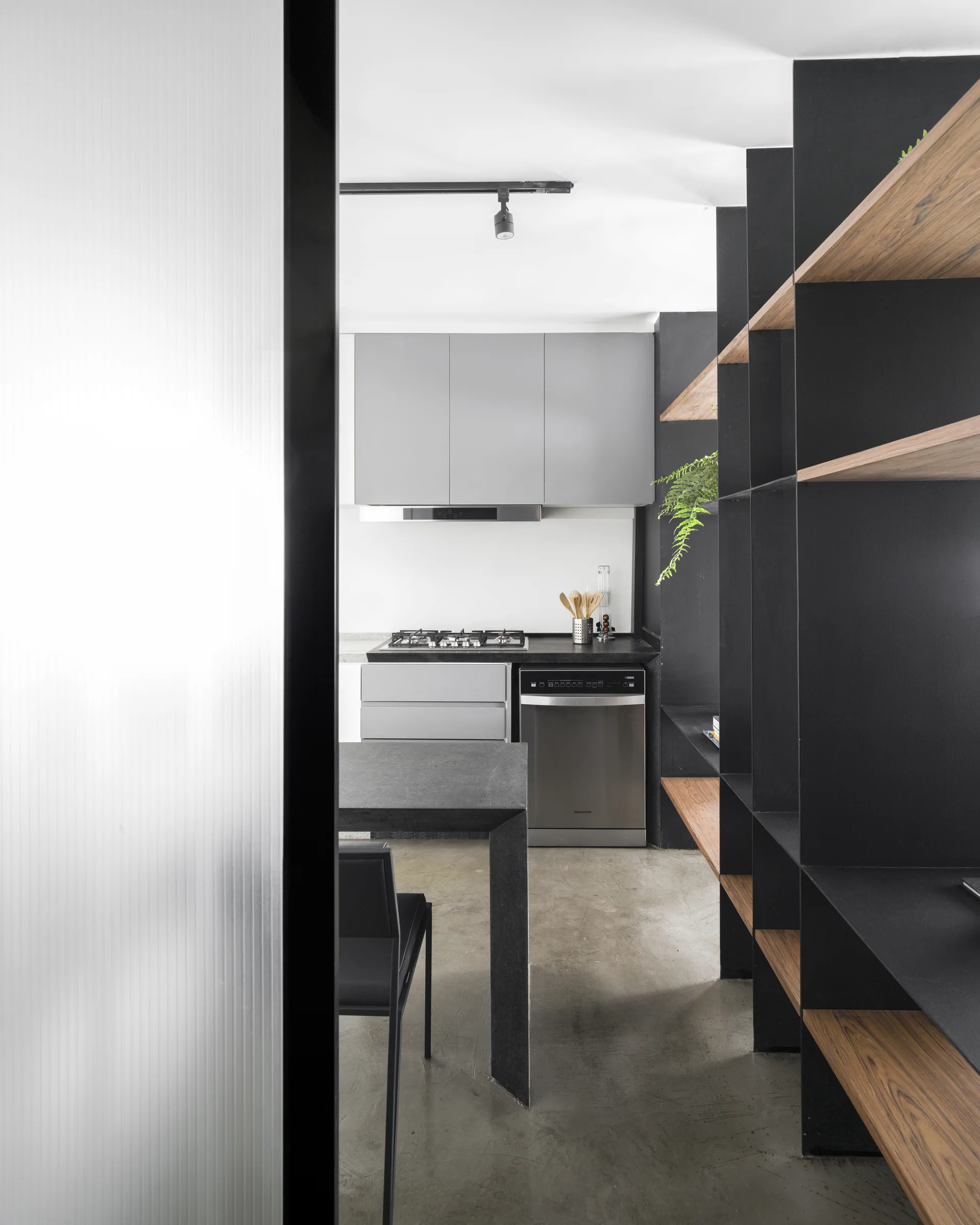 A modern kitchen featuring grey cabinetry, a tall black metal shelving unit with wood inserts, and concrete-look flooring.