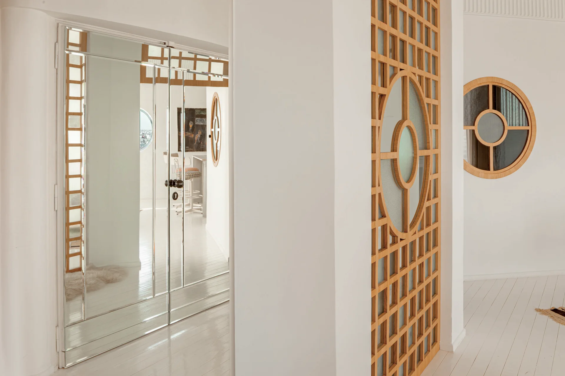 A bright white hallway features polished white wood floors, mirrored double doors, and a natural wood geometric lattice partition screen.