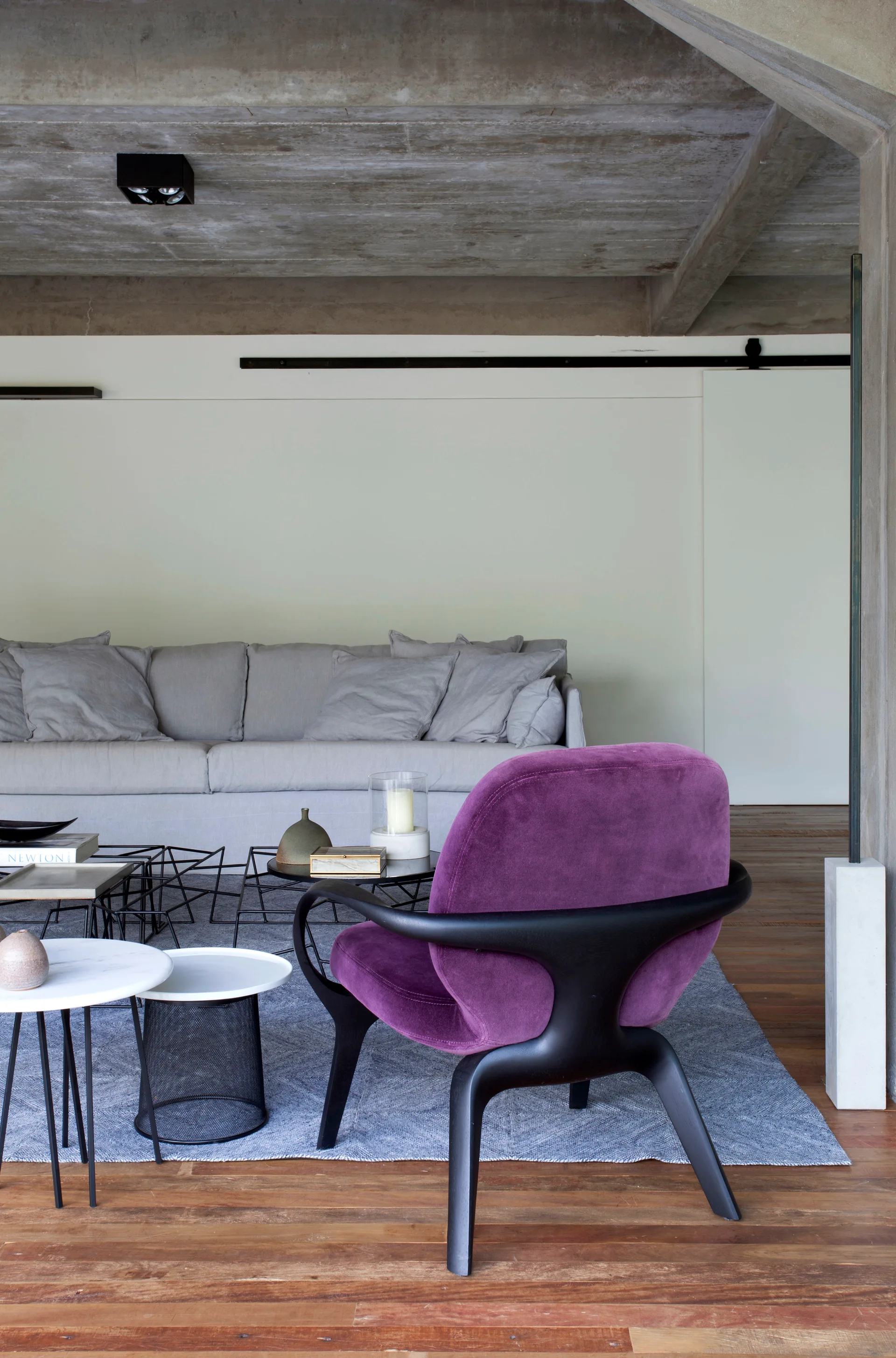 A modern living room features a low-profile grey sofa, a group of nesting coffee tables, and a vibrant purple velvet armchair on a grey rug.