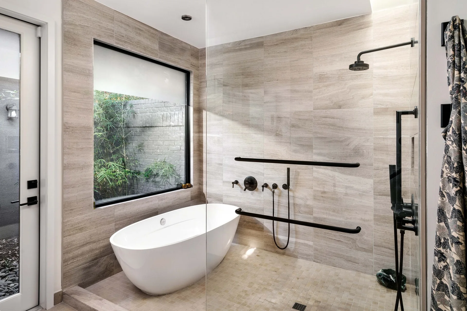 A contemporary wet room bathroom featuring a white soaking tub, beige tiled walls, and matte black shower fixtures with integrated grab bars.