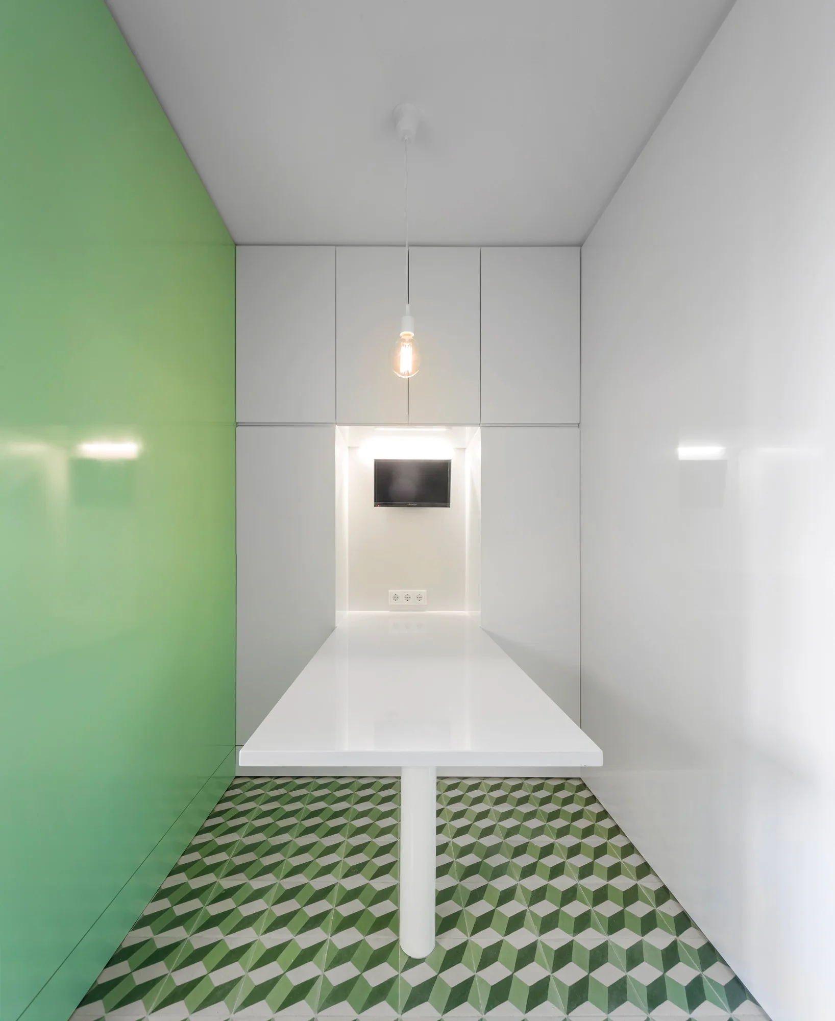 A minimalist dining alcove features a white pedestal table, white built-in cabinets, a green accent wall, and geometric cube floor tiles.