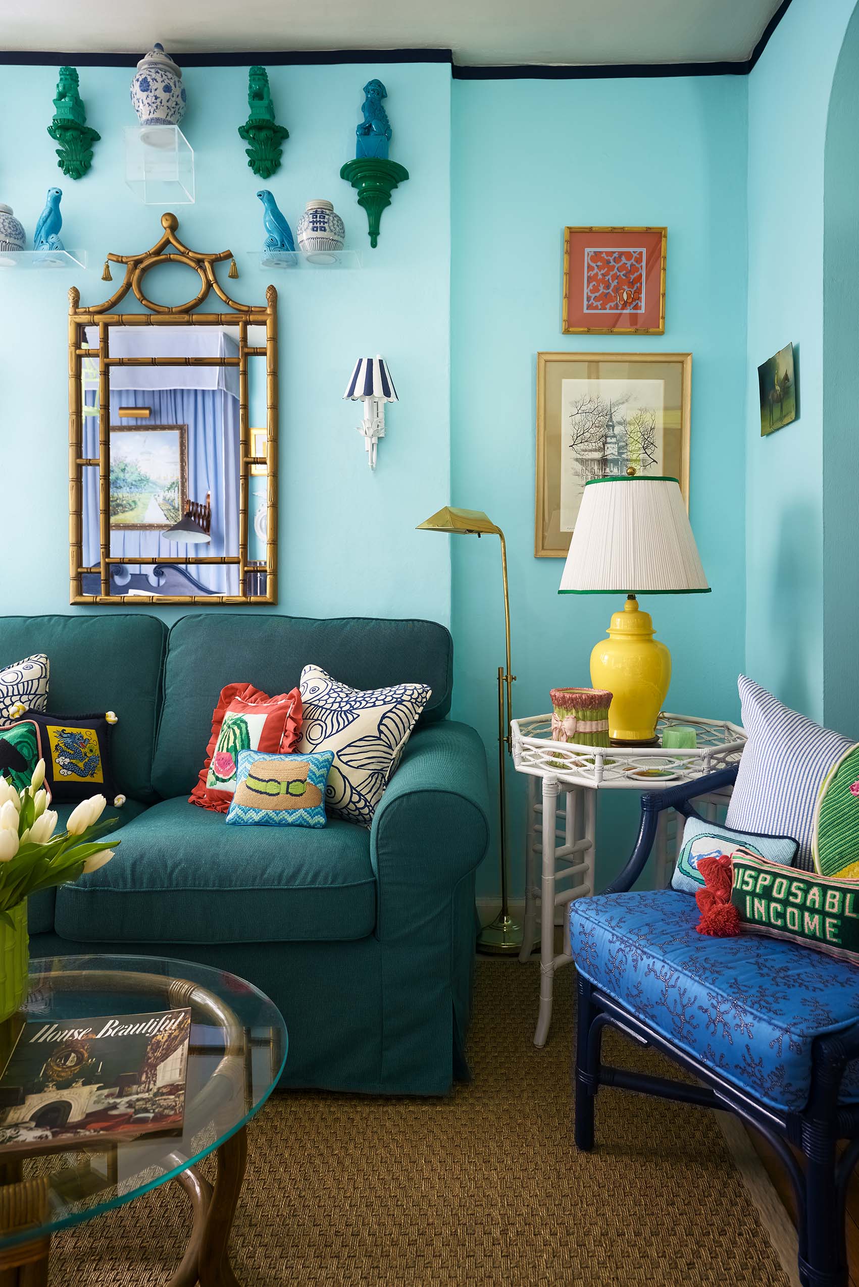 A vibrant living room corner features cyan walls, a teal sofa with patterned pillows, a blue armchair, and a gold bamboo-style mirror.