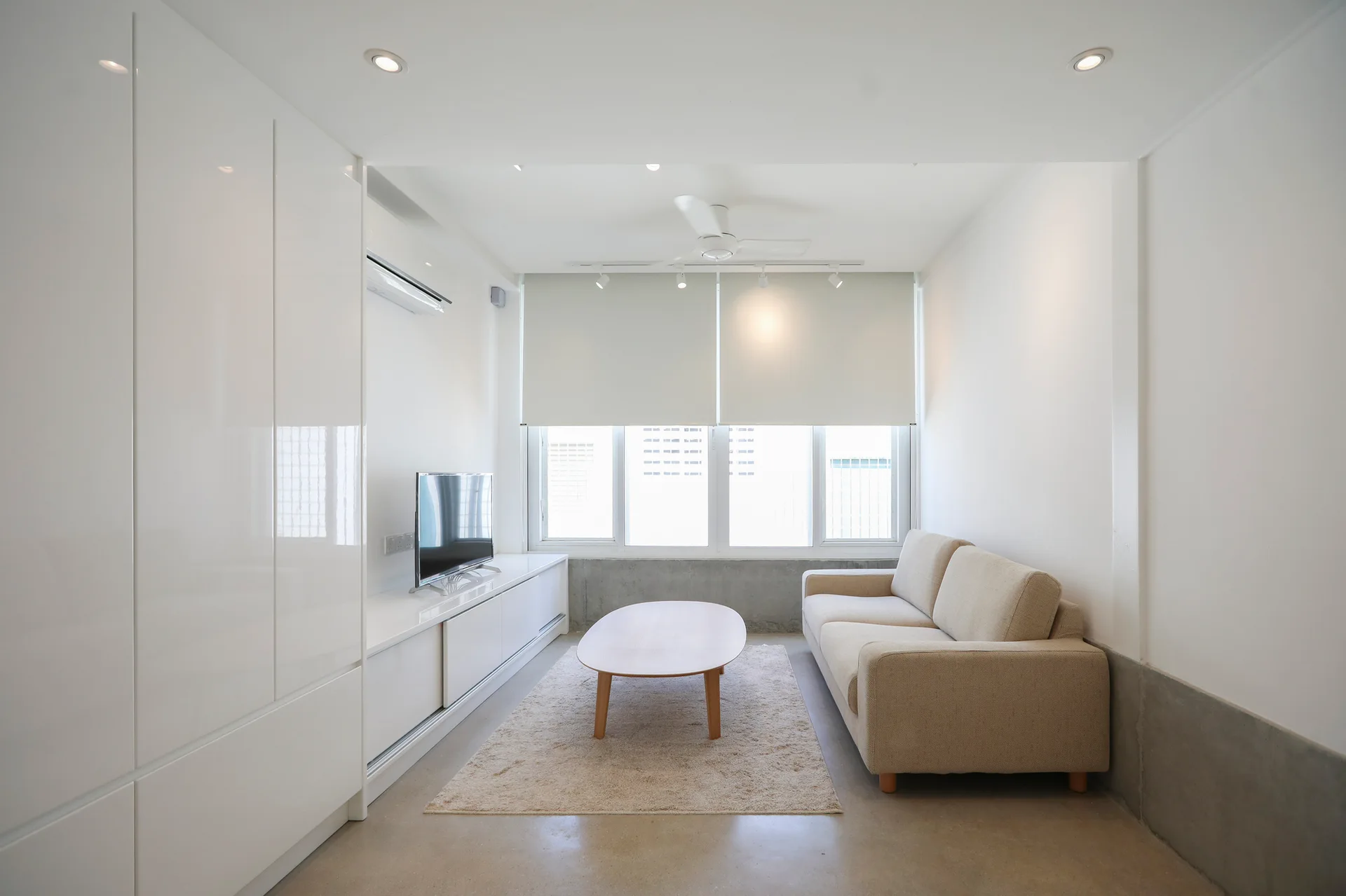 A minimalist living room features a beige fabric sofa, an oval wood coffee table, and a wall of sleek, glossy white built-in cabinets.