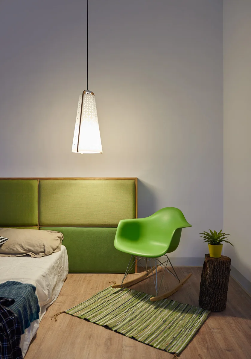 A bedroom corner features a green upholstered headboard, a green molded rocking chair, a white patterned pendant light, and a tree stump side table.