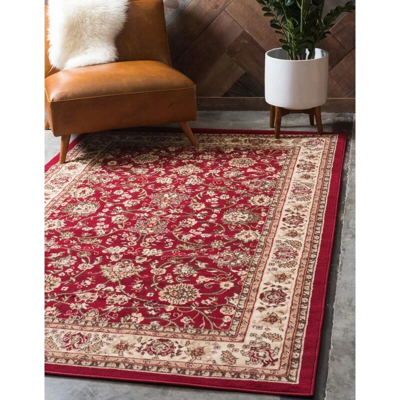 A red traditional area rug with a floral pattern lies on a concrete floor next to a leather chair and a potted plant.