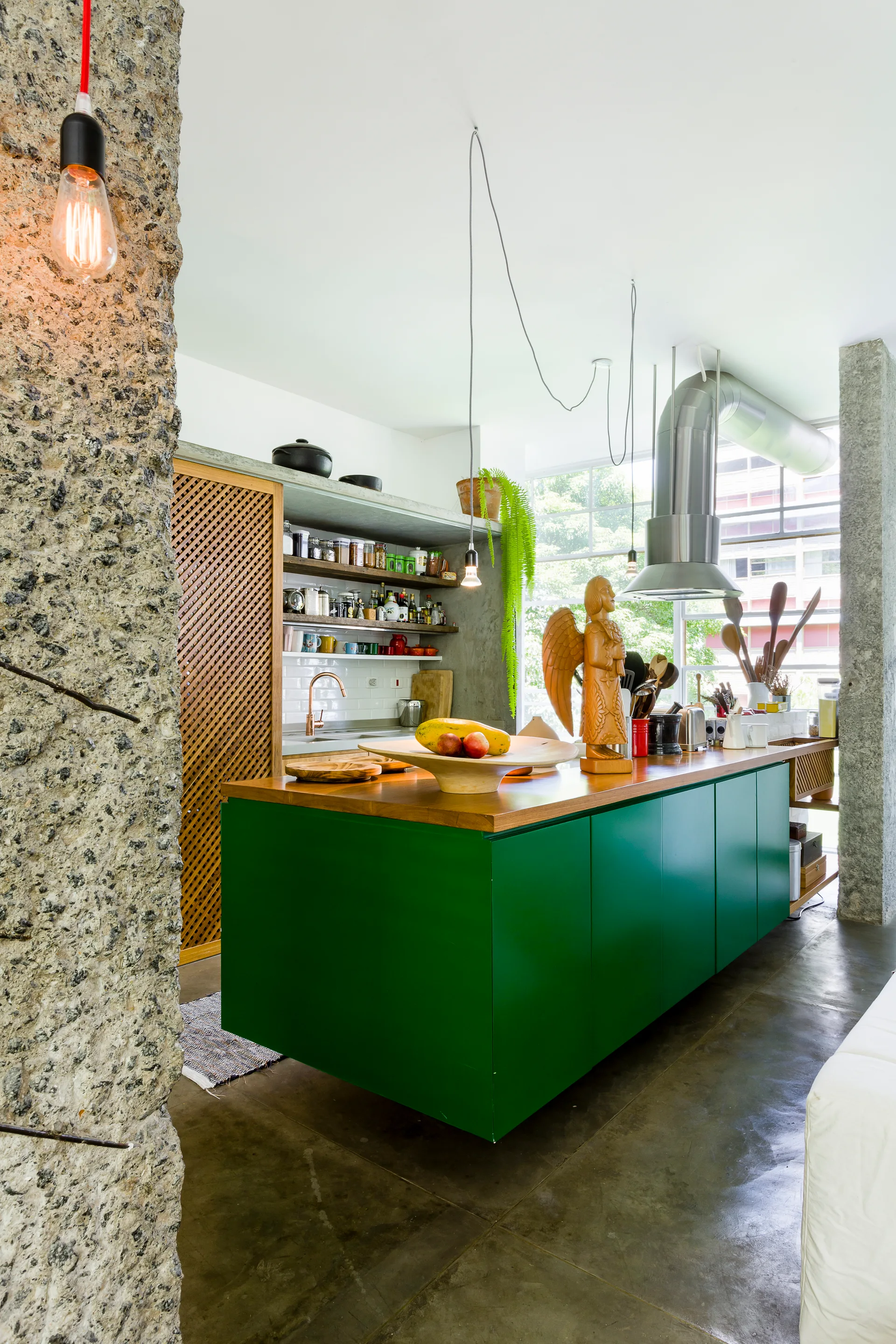A modern kitchen features a vibrant green island with a wood countertop, raw stone pillars, and open shelves.