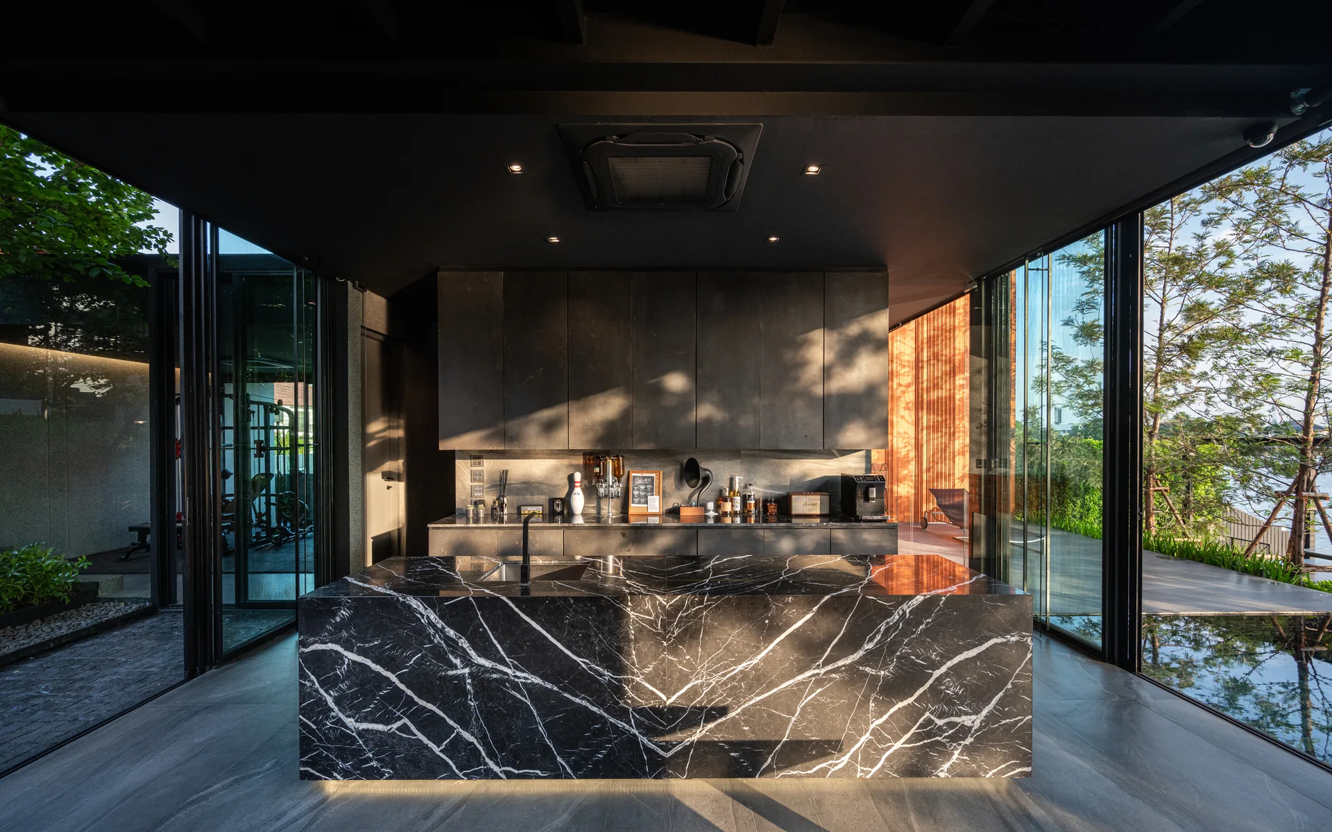 A modern dark kitchen features a large black marble island with white veining, matte black cabinetry, and floor-to-ceiling glass walls.